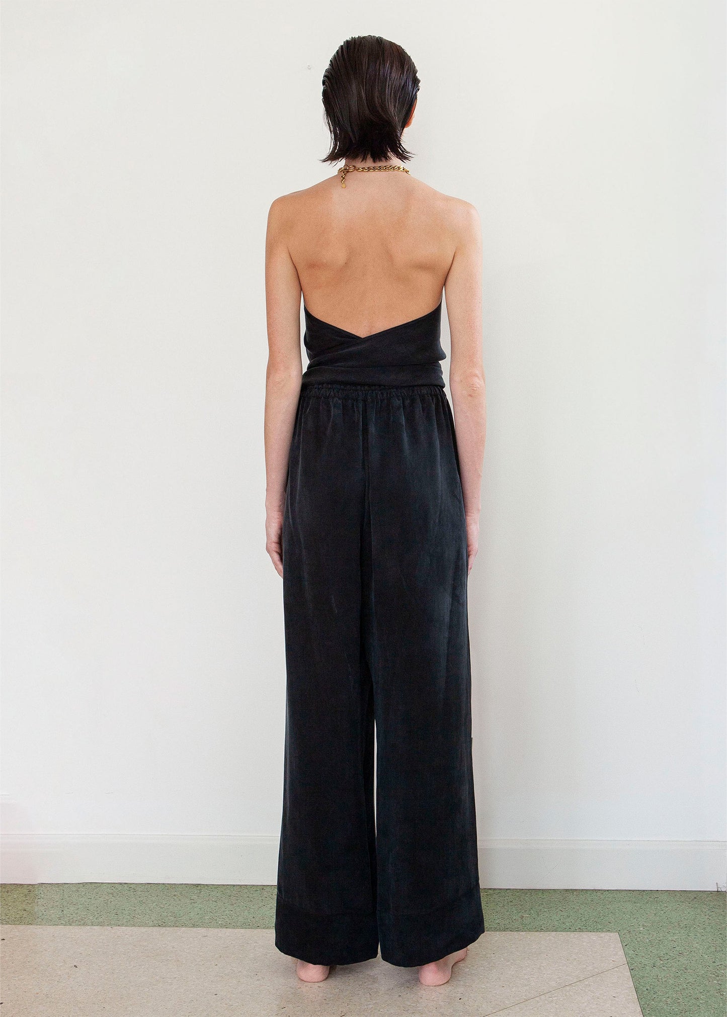 Woman wearing a luxury vegan silk black halter jumpsuit with a tied waist.