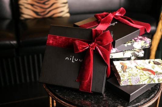 Stacked niLuu reusable gift boxes wrapped in red velvet bows and floral patterns, reflecting the brand’s luxurious vegan silk holiday gift collection.