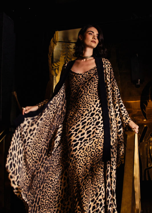  A woman models a matching niLuu leopard print silk cami dress and long kimono robe in a dark room.