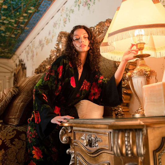 A woman in niLuu’s black silk Olivia print robe in a luxurious, richly decorated room.