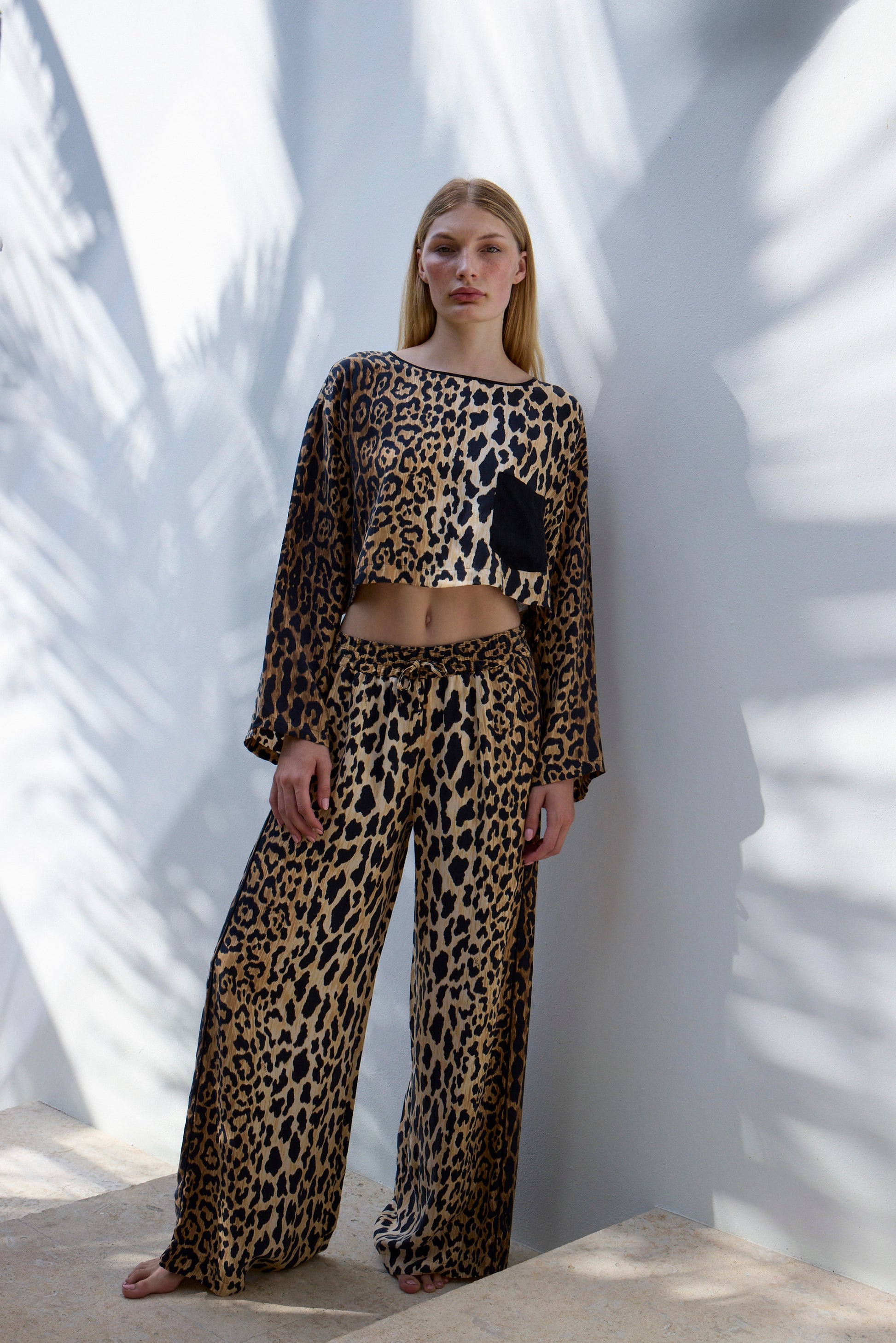 Model wearing Leo crop tee and lounge pant set against white wall