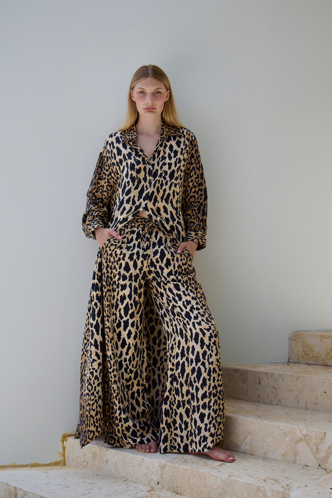 A woman in a Leo Wildesse print vegan silk lounge pants from niLuu on stone steps.