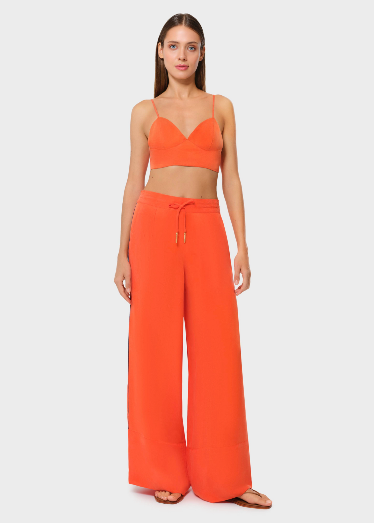 Model wearing a bright orange bralette with matching drawstring wide-leg pants, front view on studio background