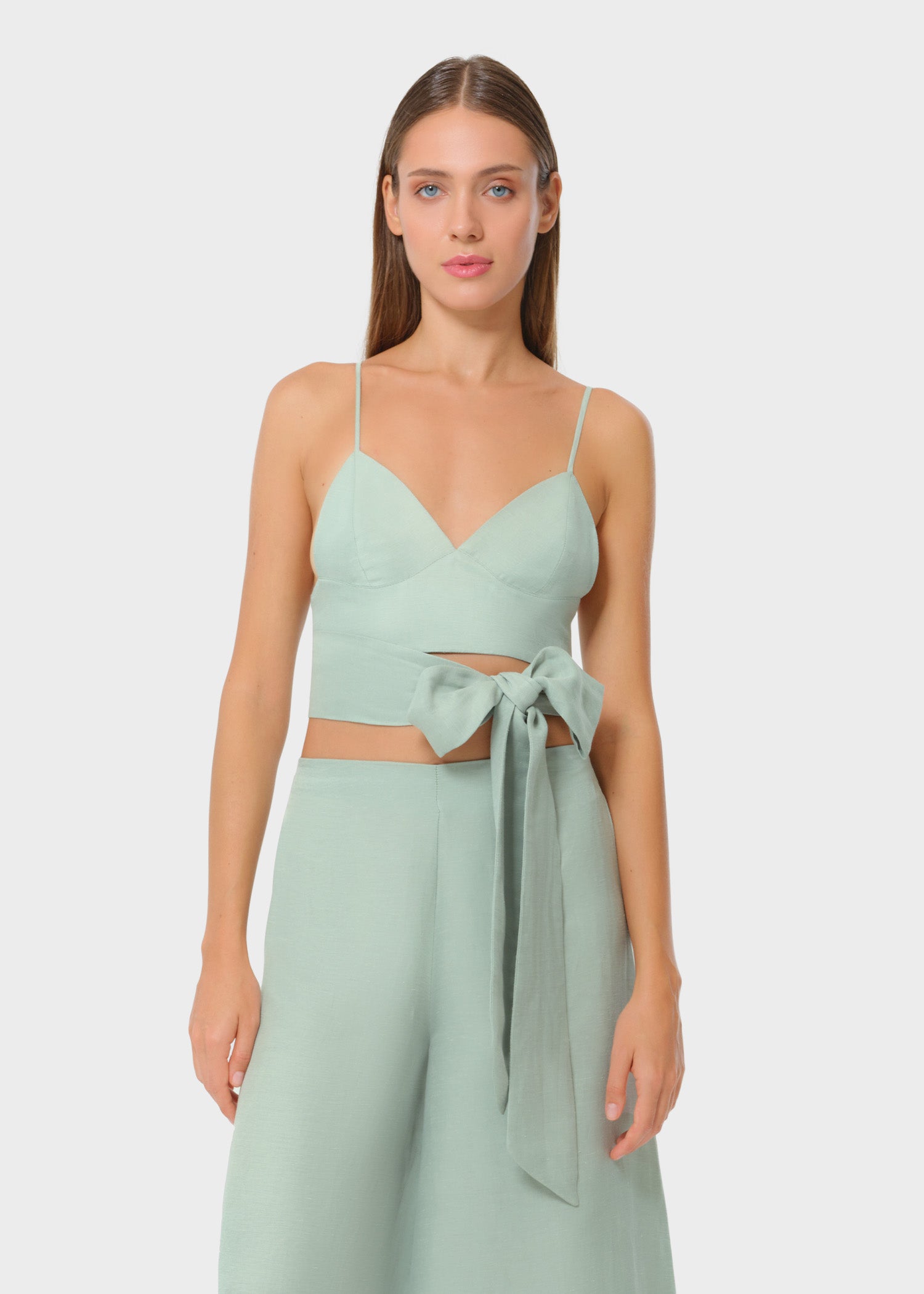 Woman wearing a luxury mint green vegan silk bralette top with spaghetti straps, paired with a matching bow-tie wrap skirt, resort wear