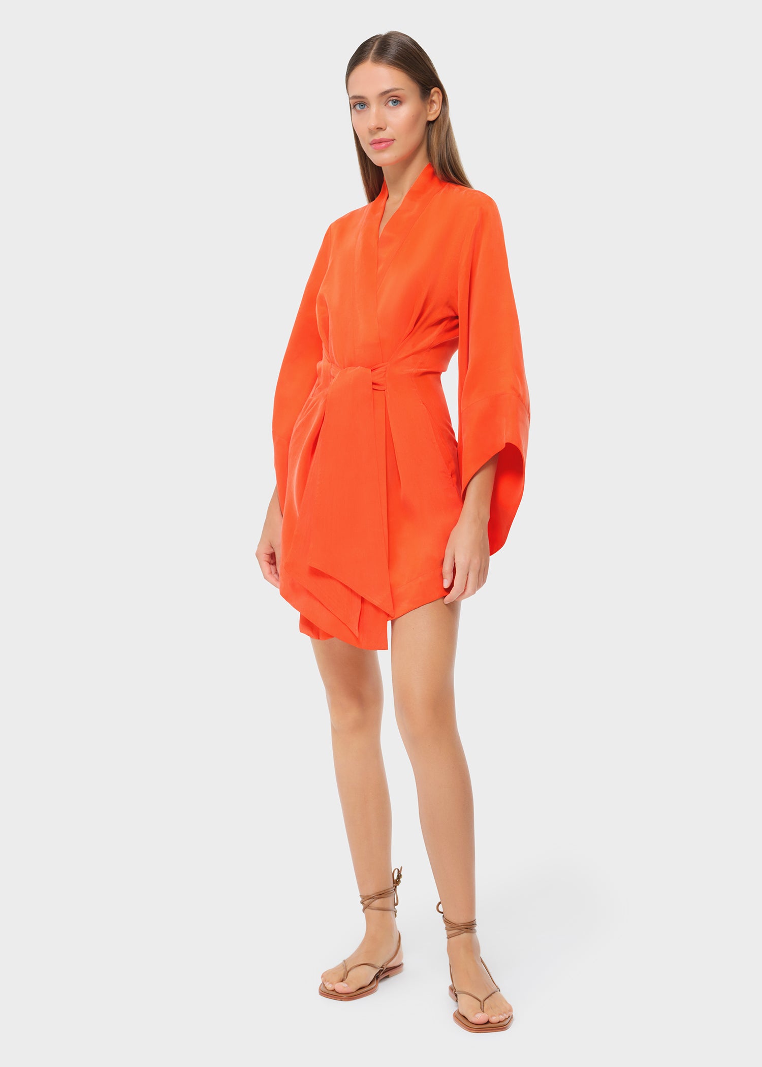 Model wearing a bright orange short wrap robe with wide sleeves and tie waist, paired with flat sandals.