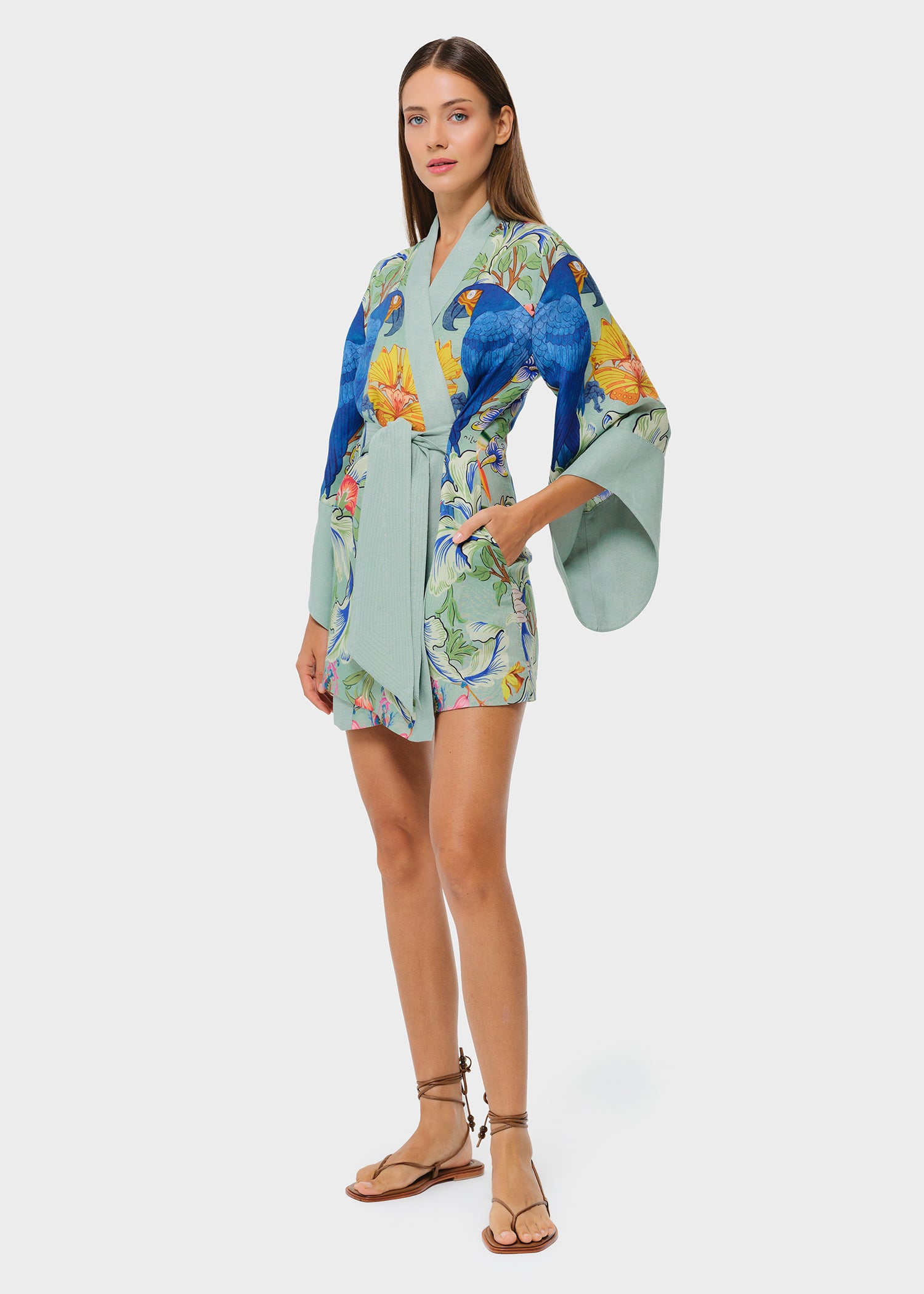 Model wearing a green tropical print short wrap robe with wide sleeves and tie waist, paired with strappy sandals on a neutral background.
