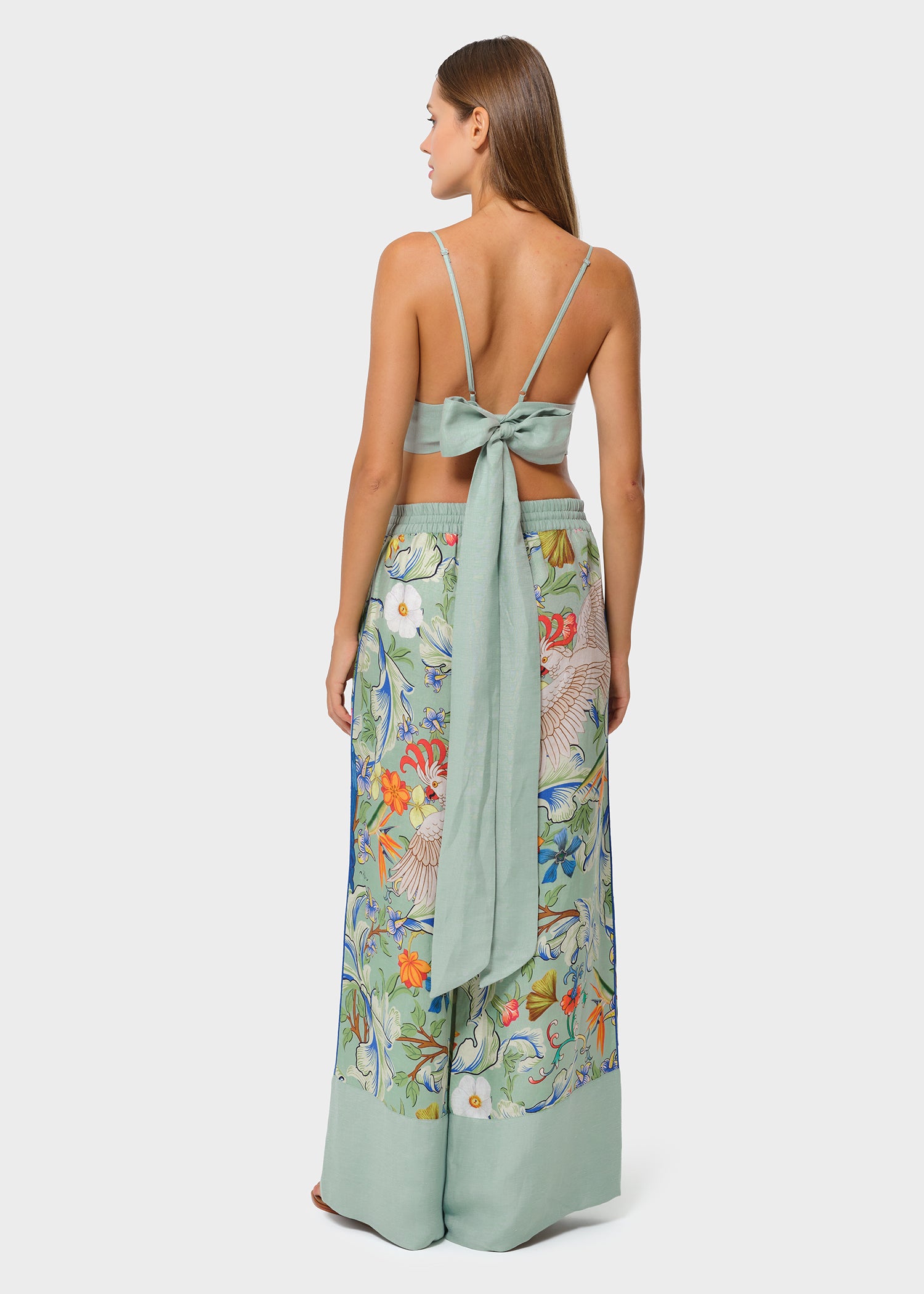 Back view of model in sage green bralette with bow tie and printed wide-leg pants on studio background