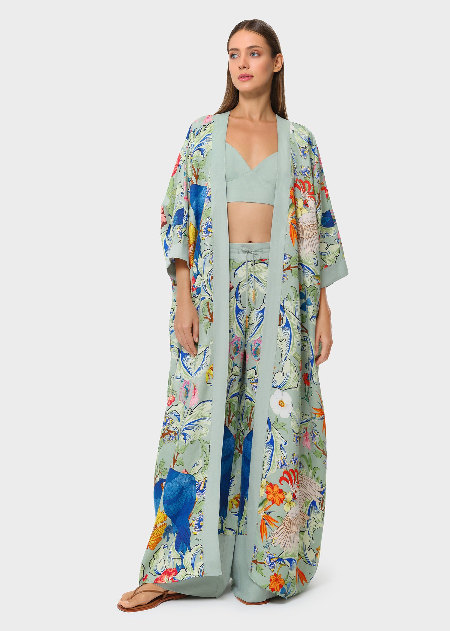 Model wearing sage green bralette with printed wide-leg pants and matching long robe on studio background