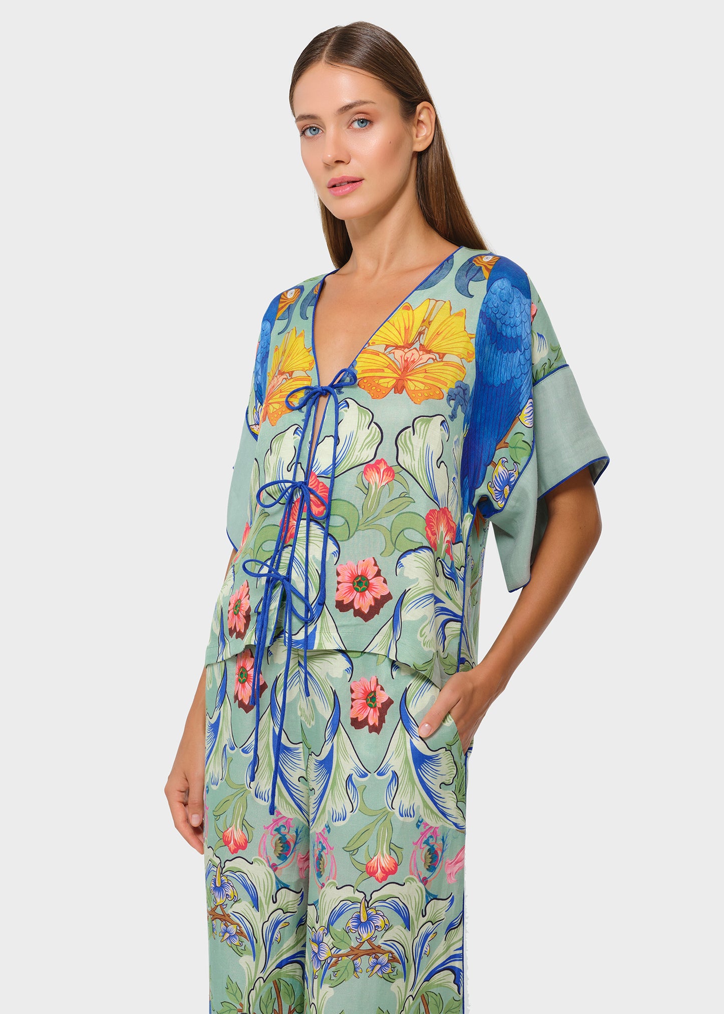 Model in tropical bird print co-ord set with V-neck tie-up top and wide-leg pants, studio shot.