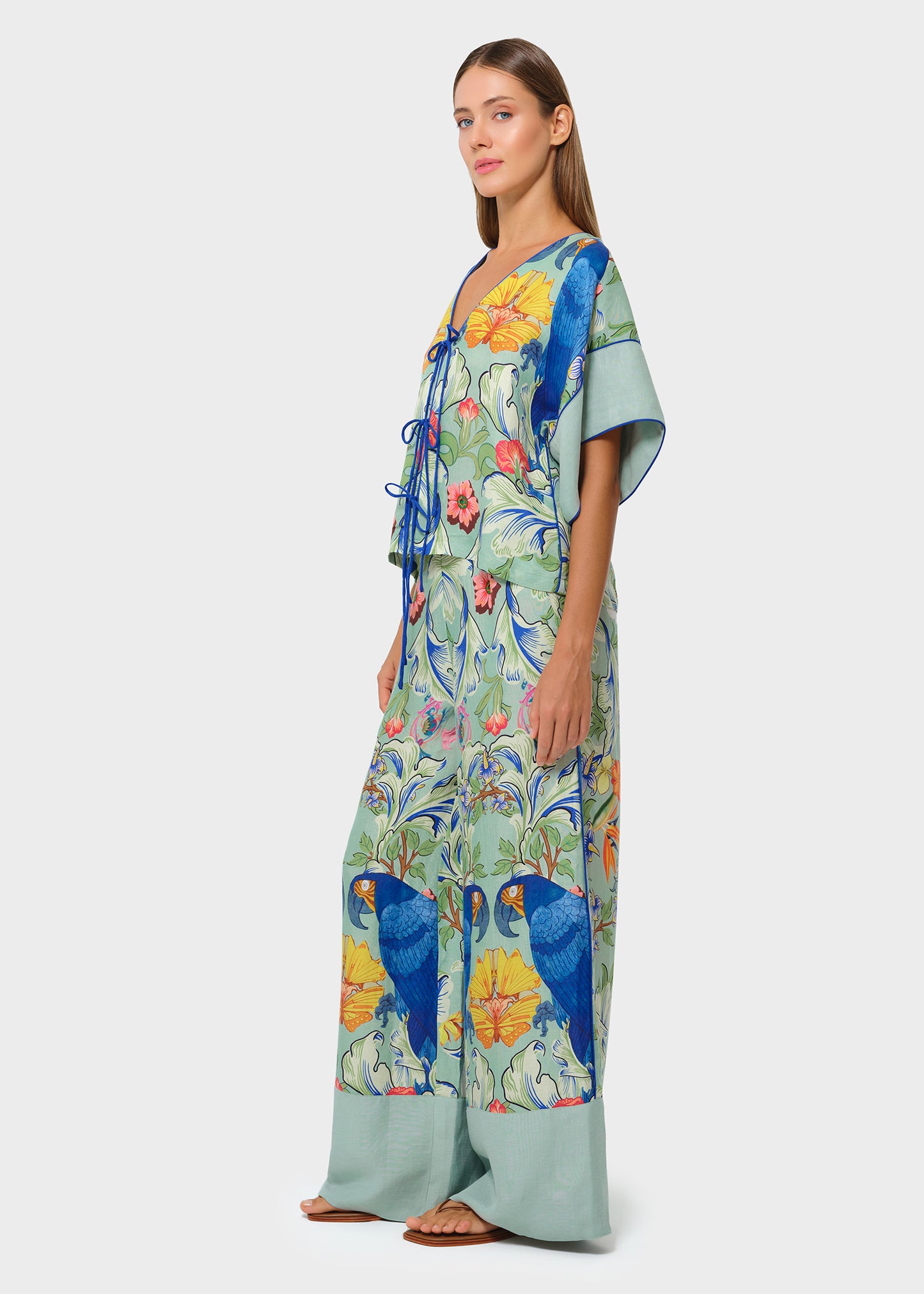 Side view of model in a tropical parrot print co-ord set featuring a tie-front blouse and wide-leg pants with soft green borders, styled against a neutral studio background.