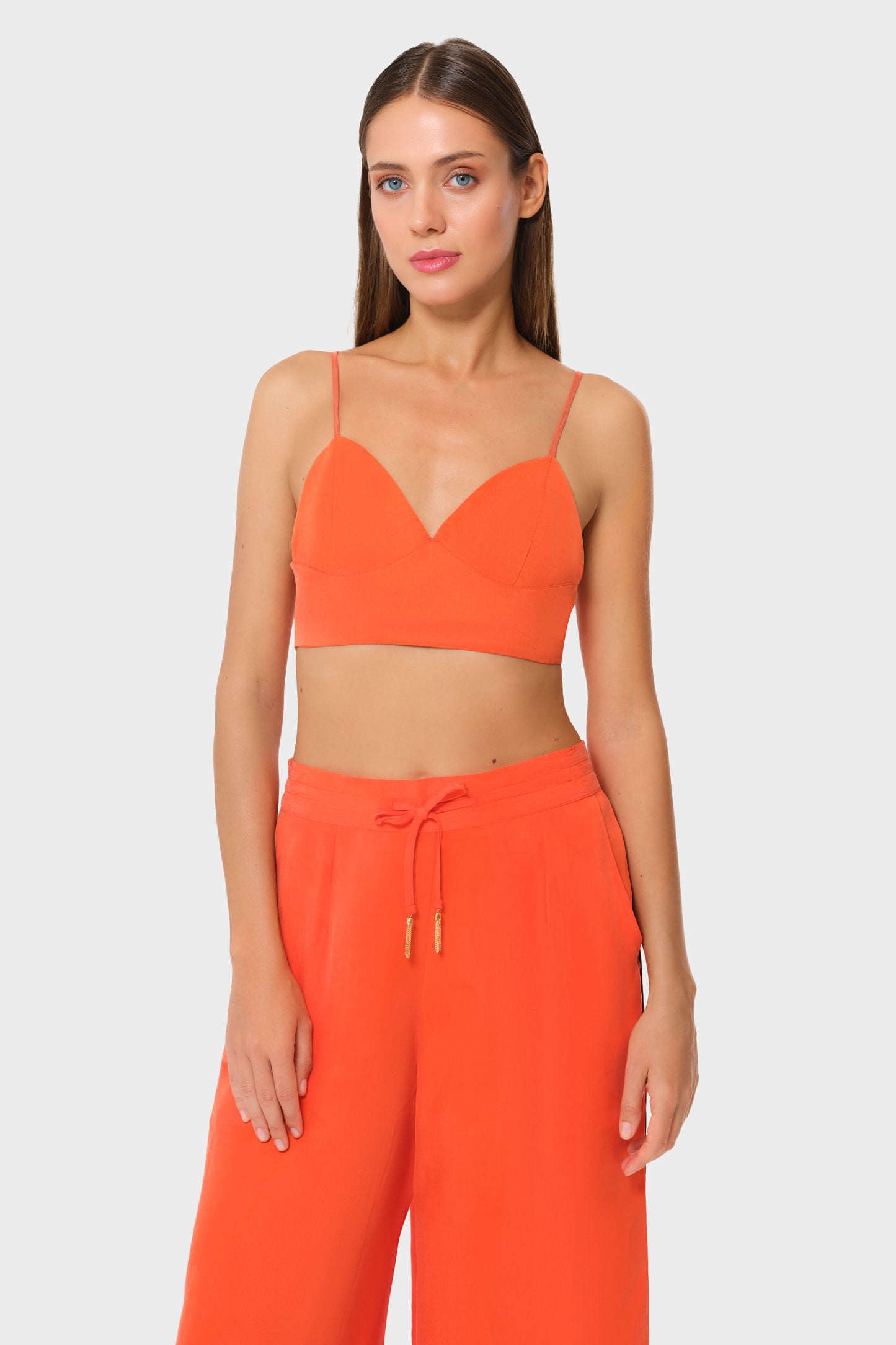 Woman wearing bright orange vegan silk bralette with matching wide leg pants, front view