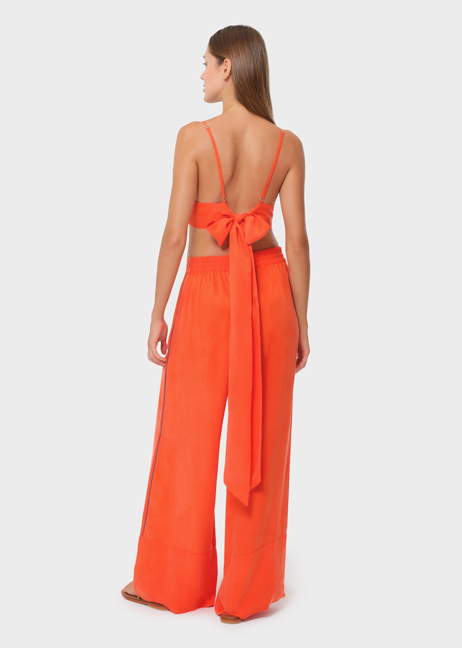 Woman wearing bright orange vegan silk bralette with bow tie back and wide leg pants