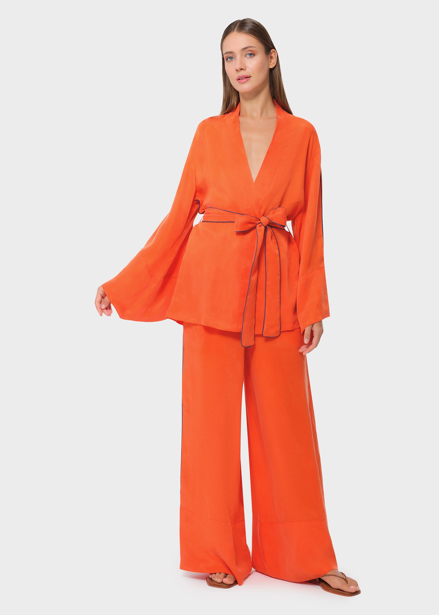 Model wearing a bright orange wrap lounge top with matching wide-leg pants, front view with tie-waist detail on studio background