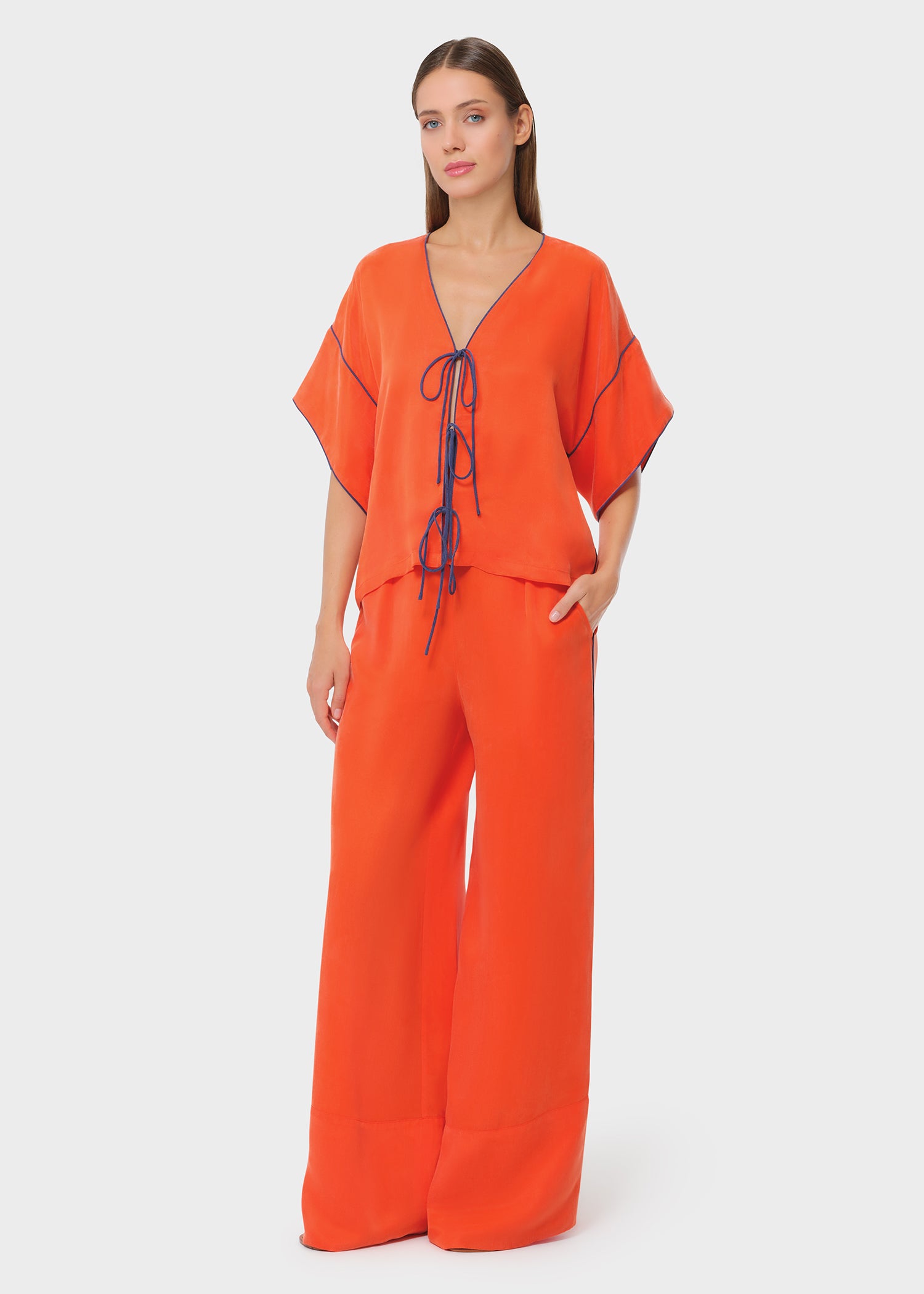 Model wearing a bright orange lounge top with matching wide-leg pants, front view with tie-front detail on studio background