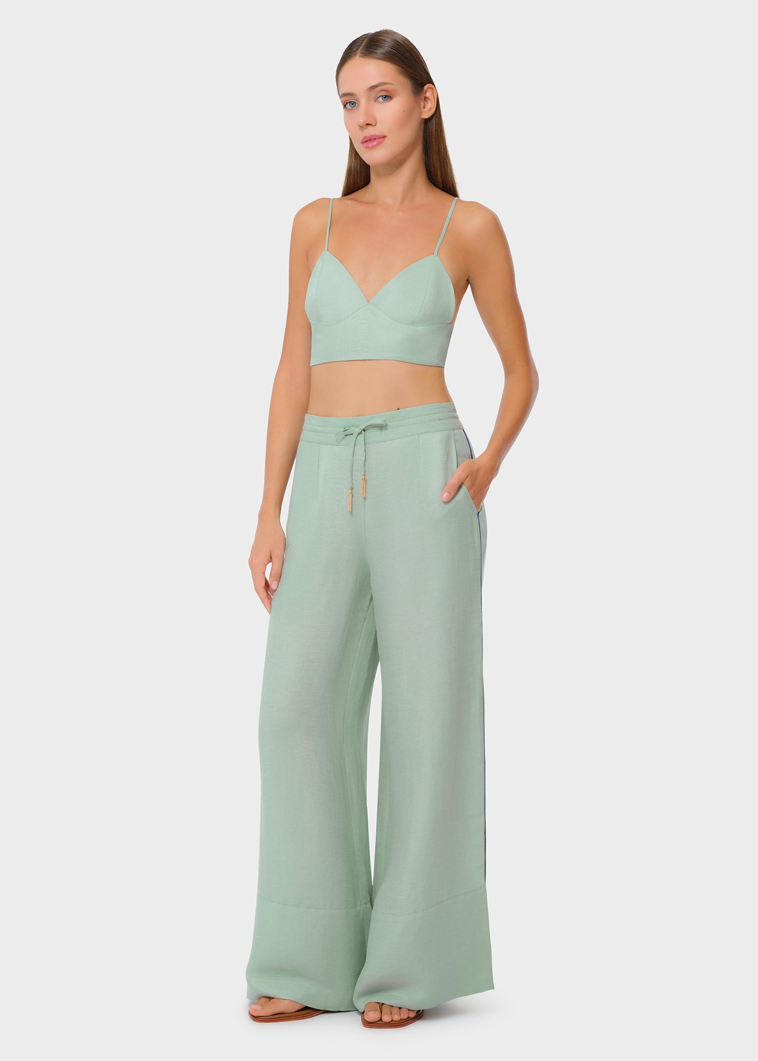 Model wearing a sage green bralette with matching drawstring wide-leg pants, front view with hand in pocket on studio background