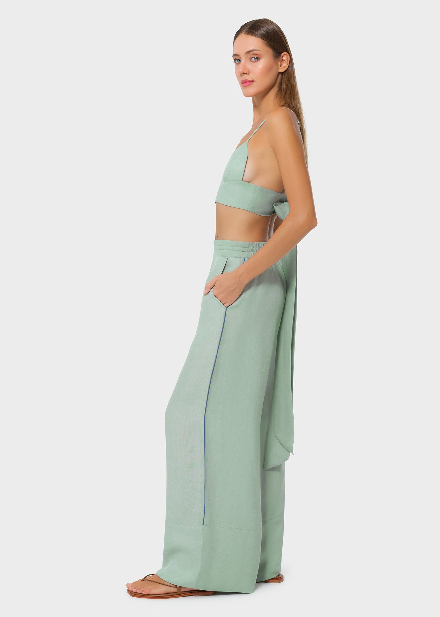 Model wearing a sage green bralette with matching drawstring wide-leg pants, side view with hand in pocket on studio background