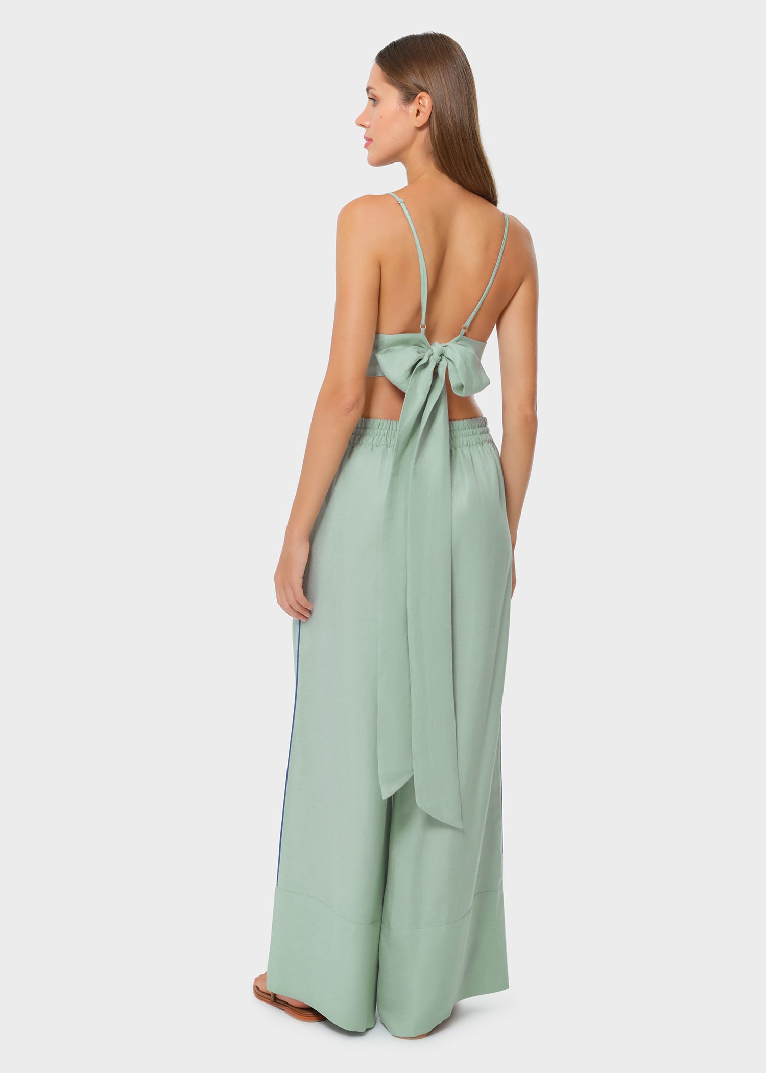 Model wearing a sage green bralette with matching drawstring wide-leg pants, three-quarter side view with hand in pocket on studio background