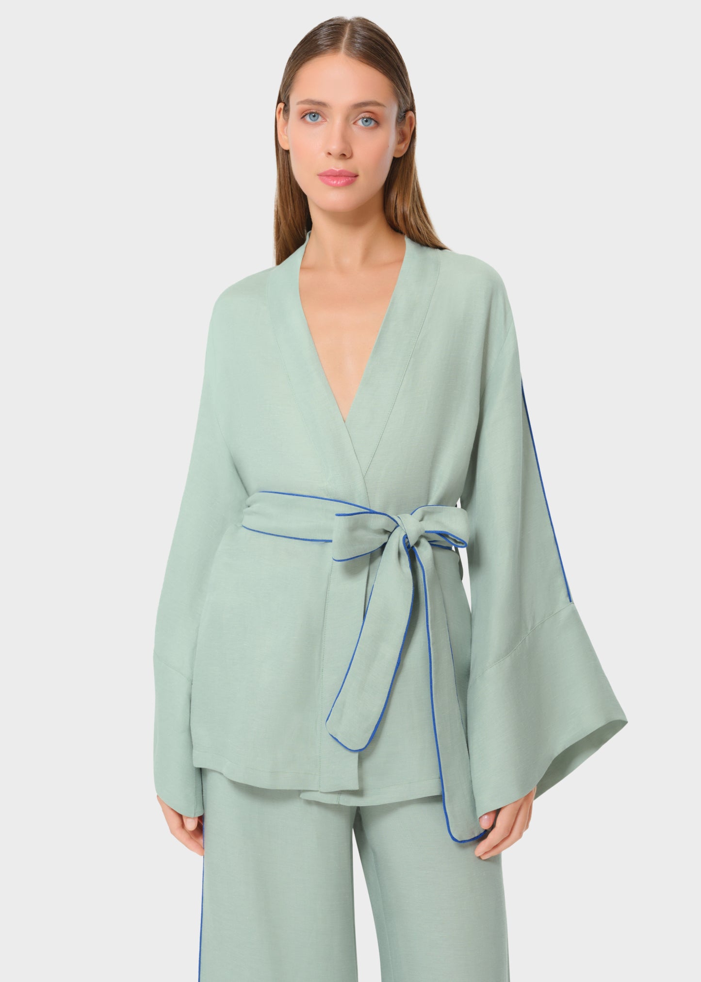 Woman wearing mint green wrap top with wide sleeves and matching pants, featuring blue piping detail and a waist tie belt, studio background