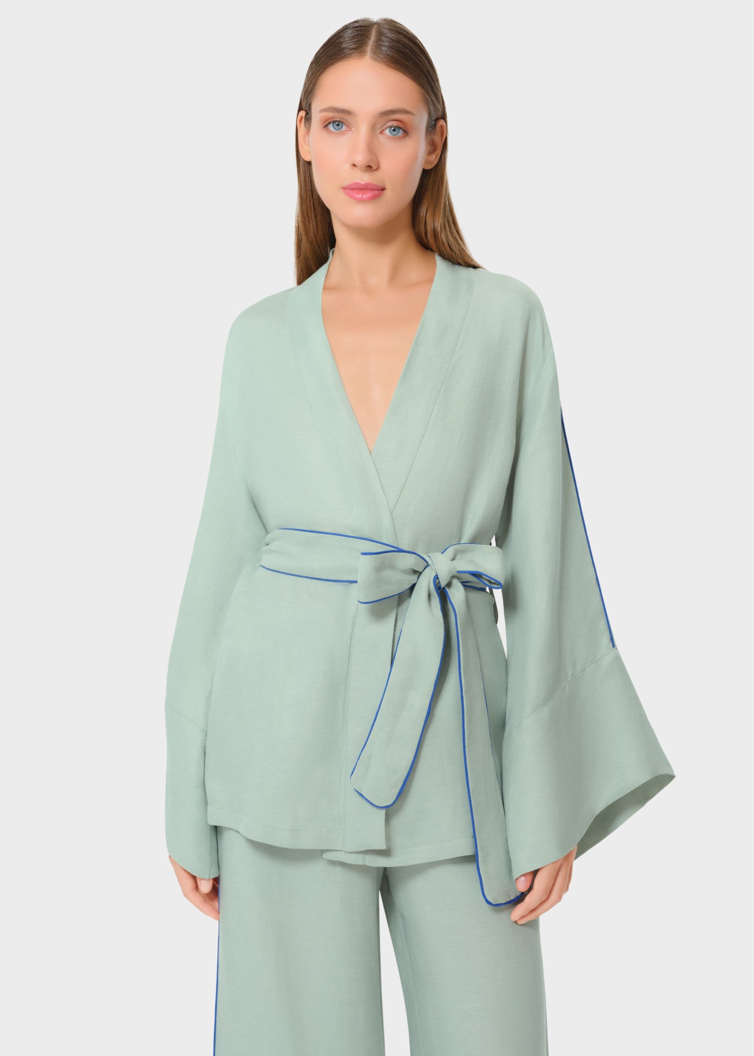 Woman wearing mint green wrap top with wide sleeves and matching pants, featuring blue piping detail and a waist tie belt, studio background