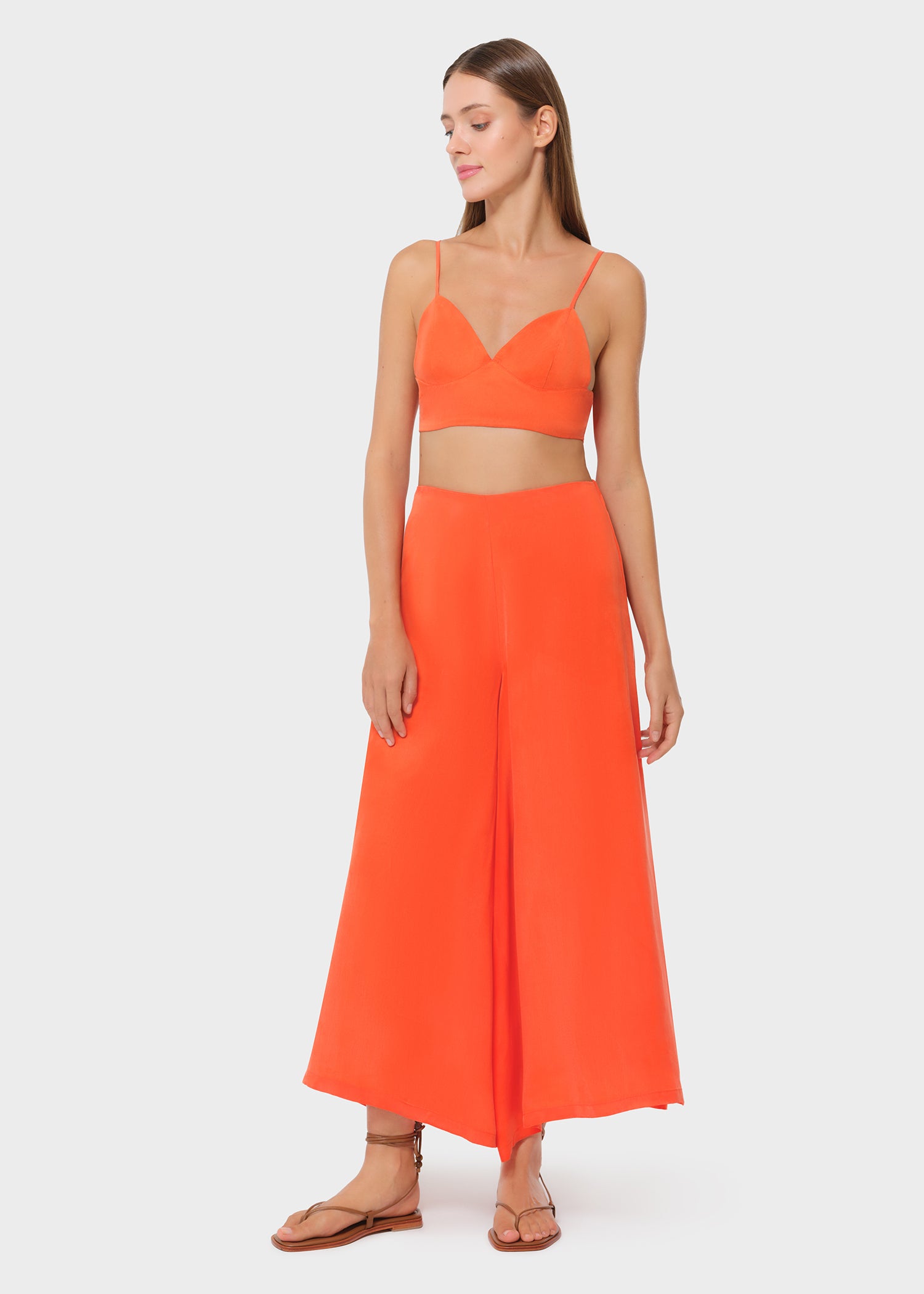 Model wearing a bright orange bralette with matching high-waisted wide-leg pants, front view on studio background