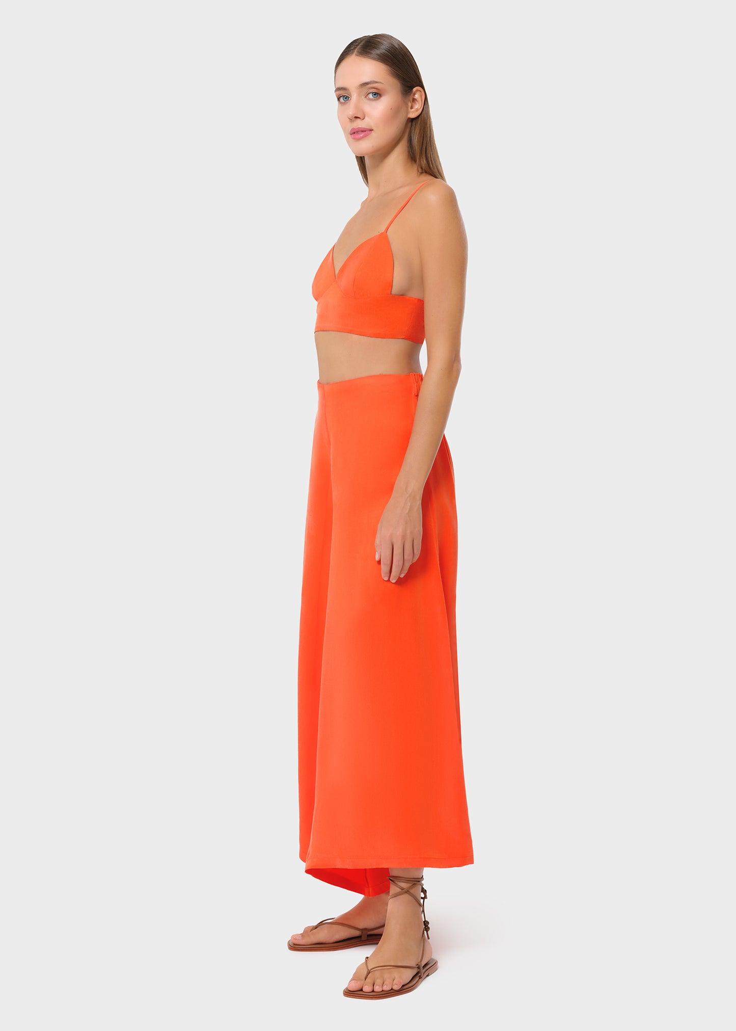 Model wearing a bright orange bralette with matching high-waisted wide-leg pants, side view on studio background