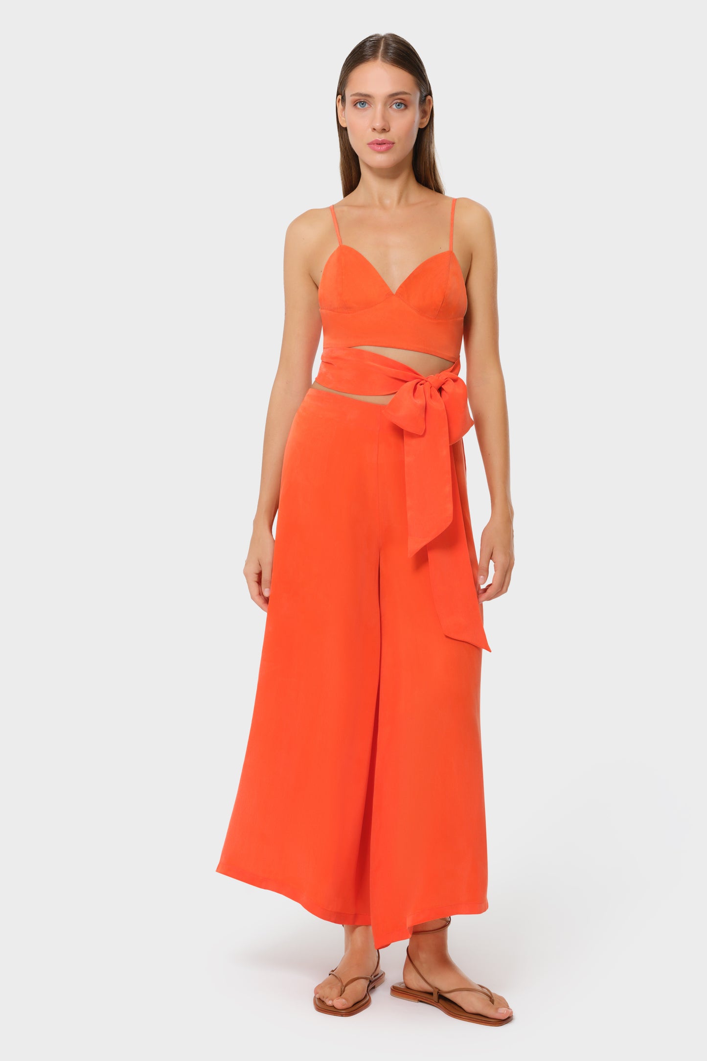 Model wearing a bright orange bralette with matching high-waisted wide-leg pants, front view with side bow detail on studio background