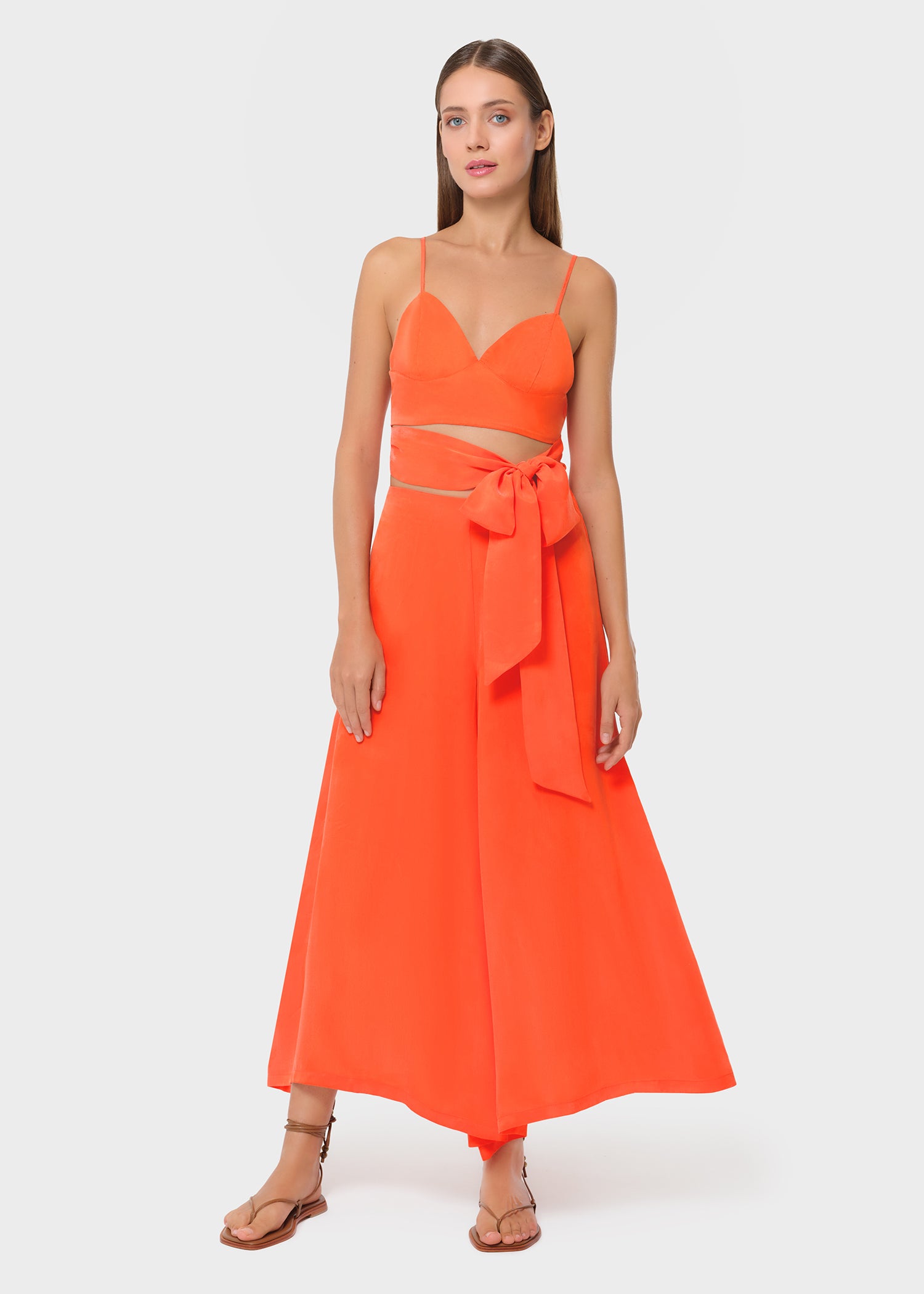 Woman wearing bright orange vegan silk bralette and bow tie maxi skirt, full length view