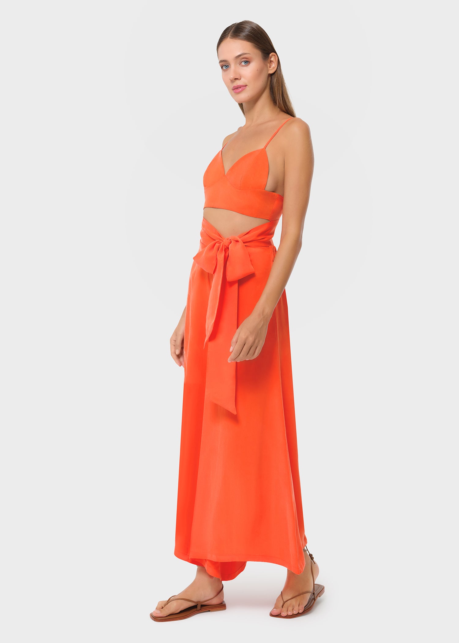 Woman wearing bright orange vegan silk bralette and bow tie maxi skirt, side view