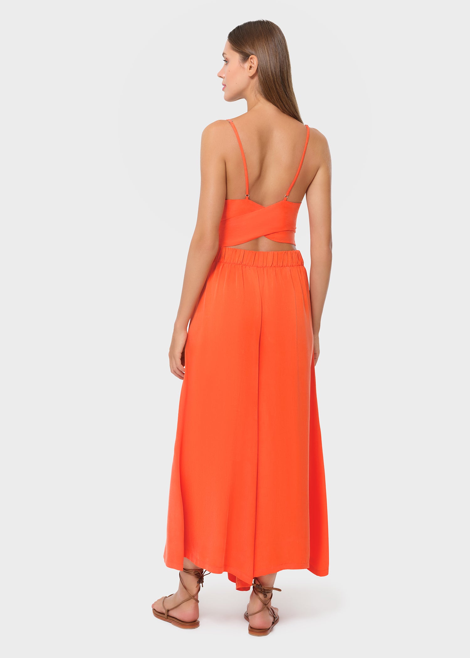 Woman wearing bright orange vegan silk bralette and maxi skirt, back view