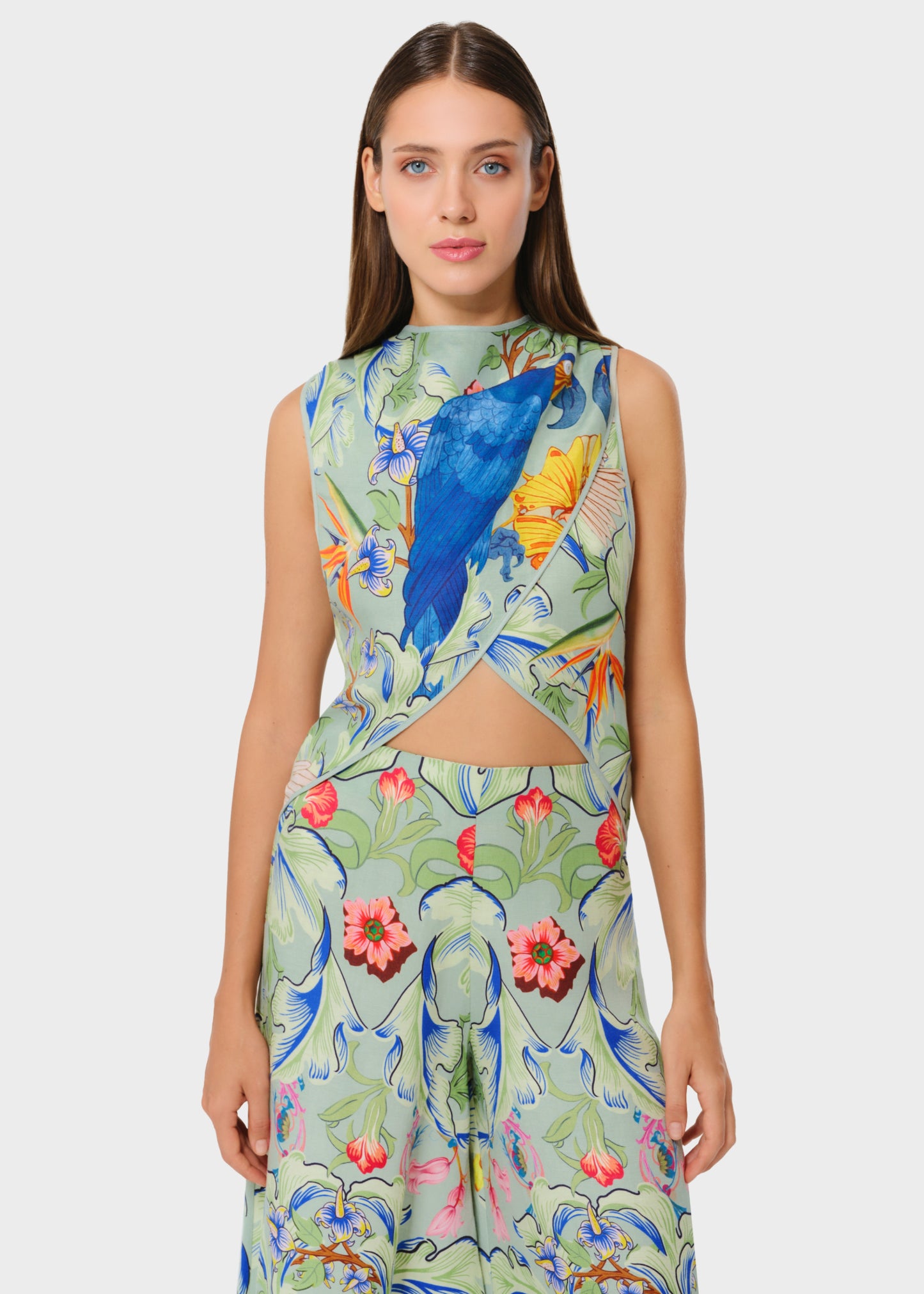 Front view of the sleeveless top and wide-leg pants in a sage base with bold floral and blue bird print. Features a soft crossover detail with a subtle waist cutout for a statement look.