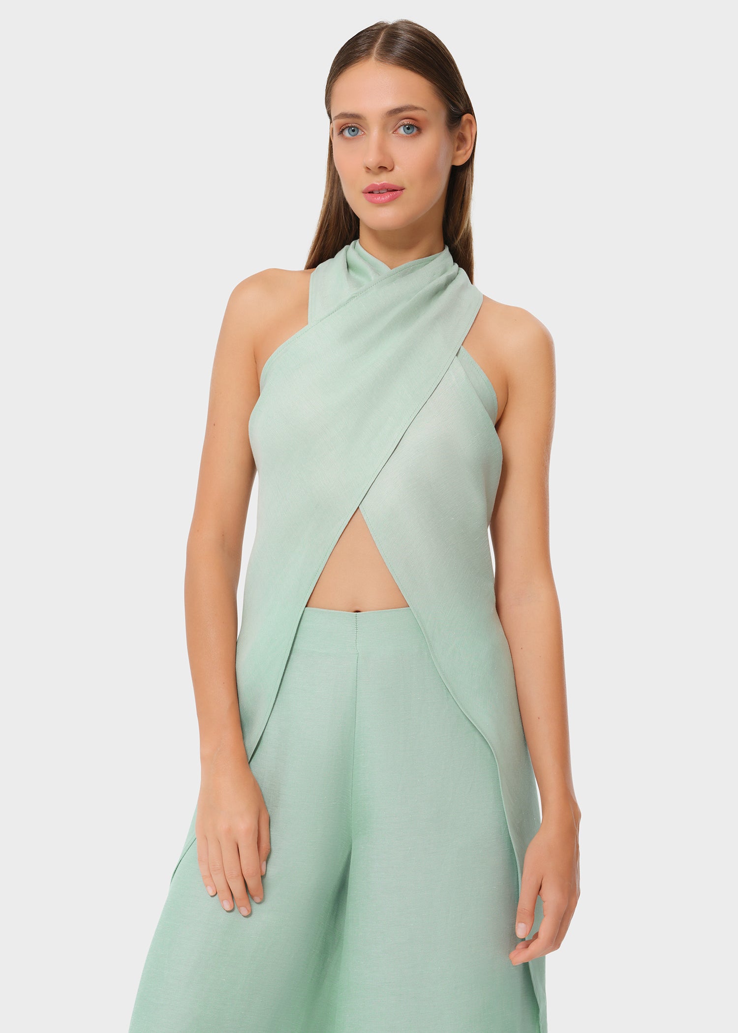 Woman wearing mint green vegan silk halter wrap top with matching wide leg pants, studio front view