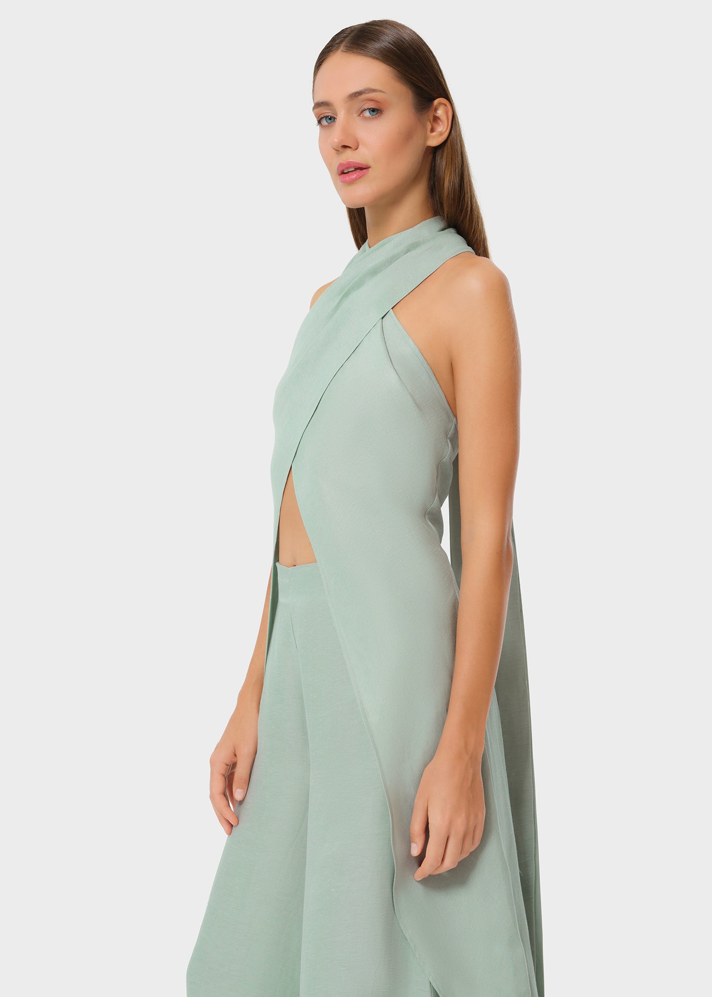 Woman wearing mint green vegan silk halter wrap top with matching wide leg pants, side studio view