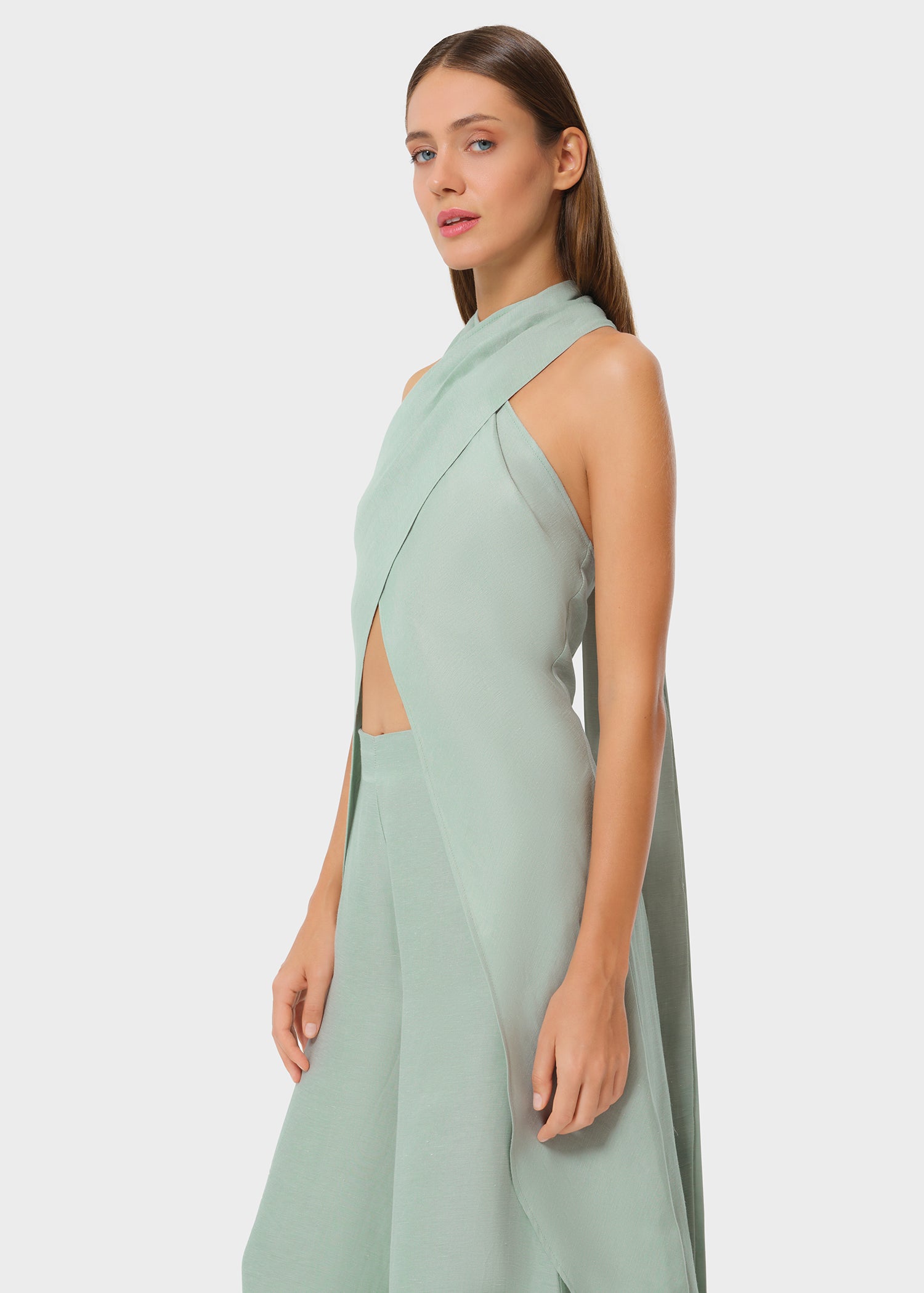 Woman wearing mint green vegan silk halter wrap top with matching wide leg pants, side studio view