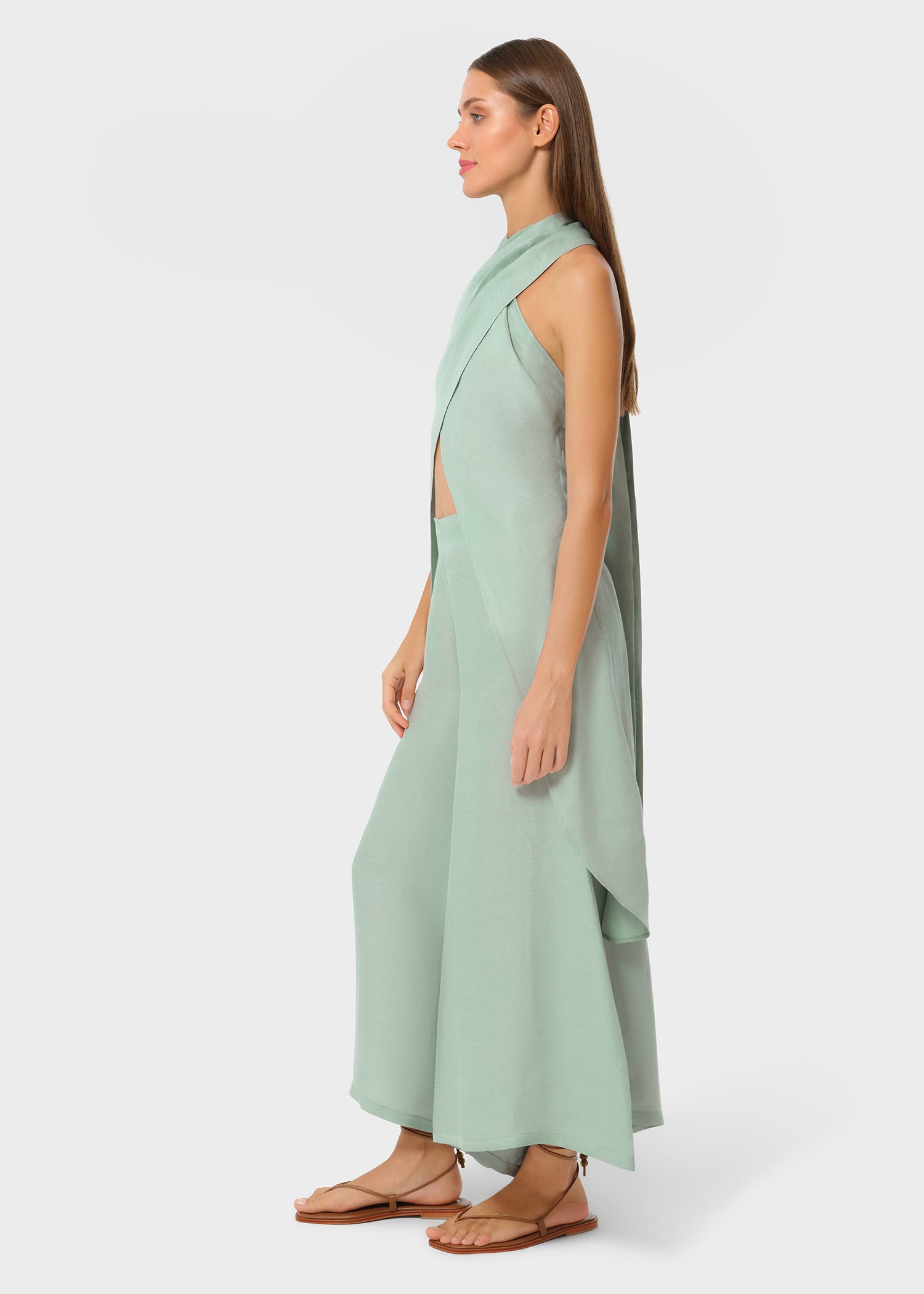 Woman wearing mint green vegan silk halter wrap top with matching wide leg pants and flat sandals, side profile studio view