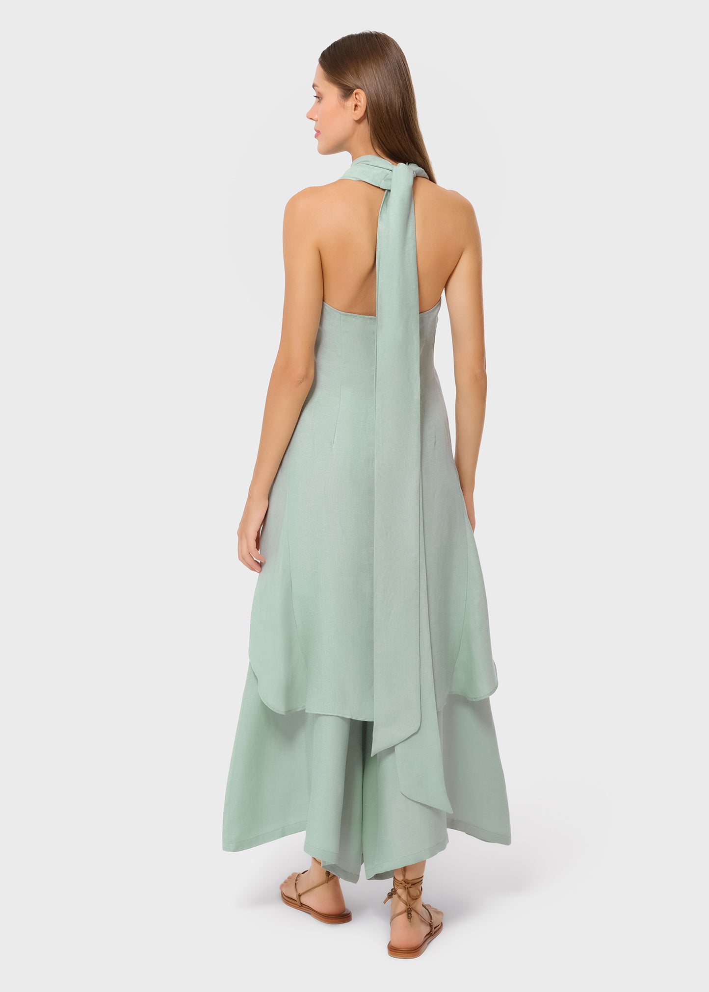 Woman wearing mint green vegan silk halter wrap top with matching wide leg pants, back view with draped scarf detail and flat sandals