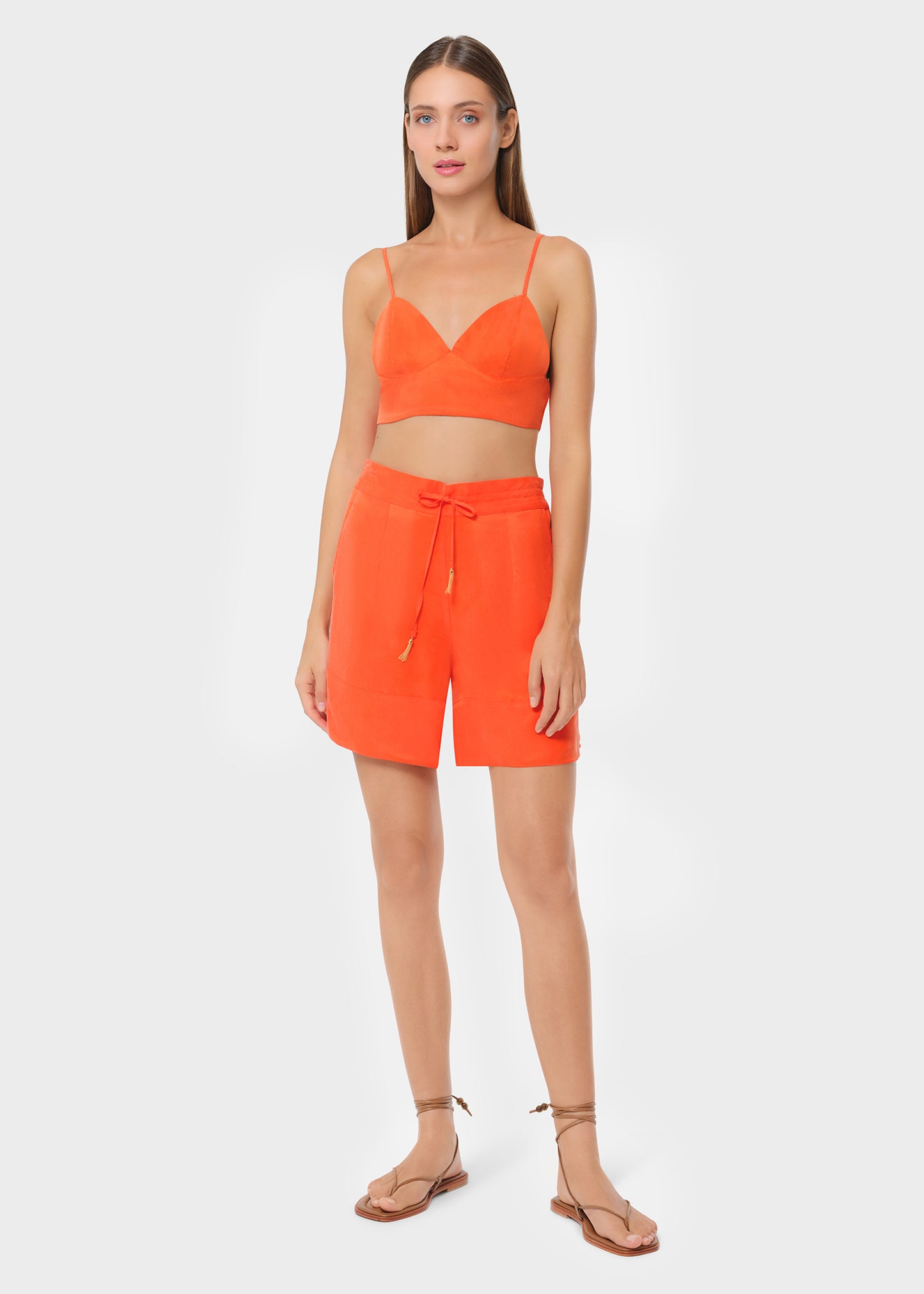 Model in bright orange bralette with matching lounge shorts, studio background