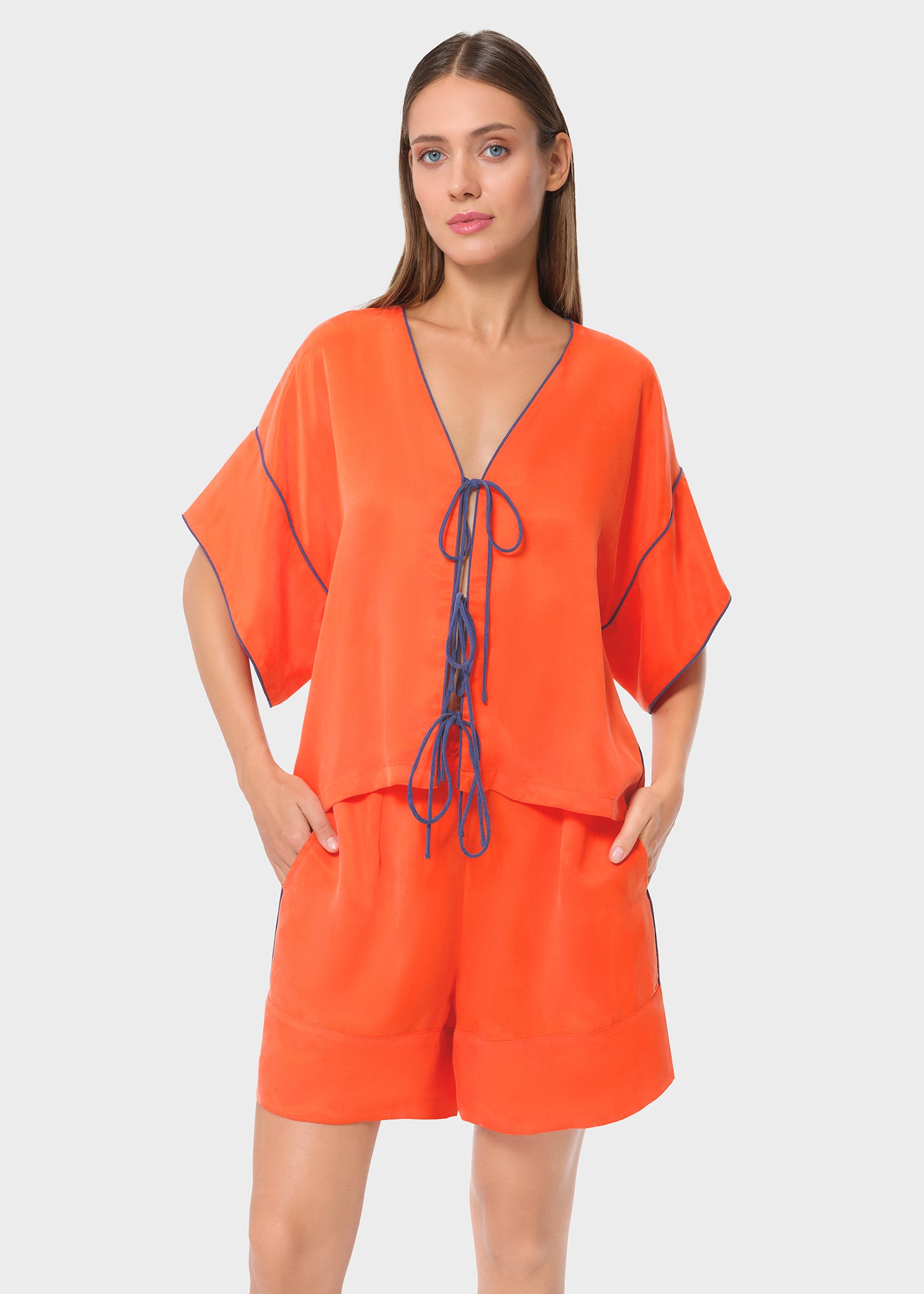 Model in bright orange tie-front top with matching lounge shorts, studio background