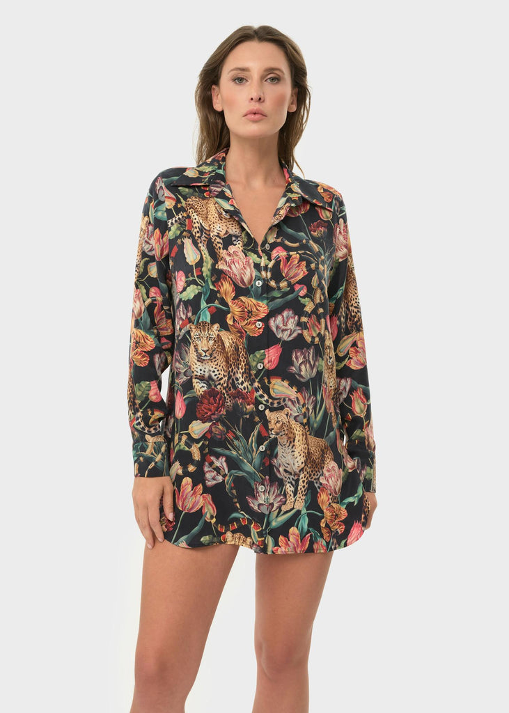 Woman wearing a floral button-up shirt with leopards and snakes on a dark background.