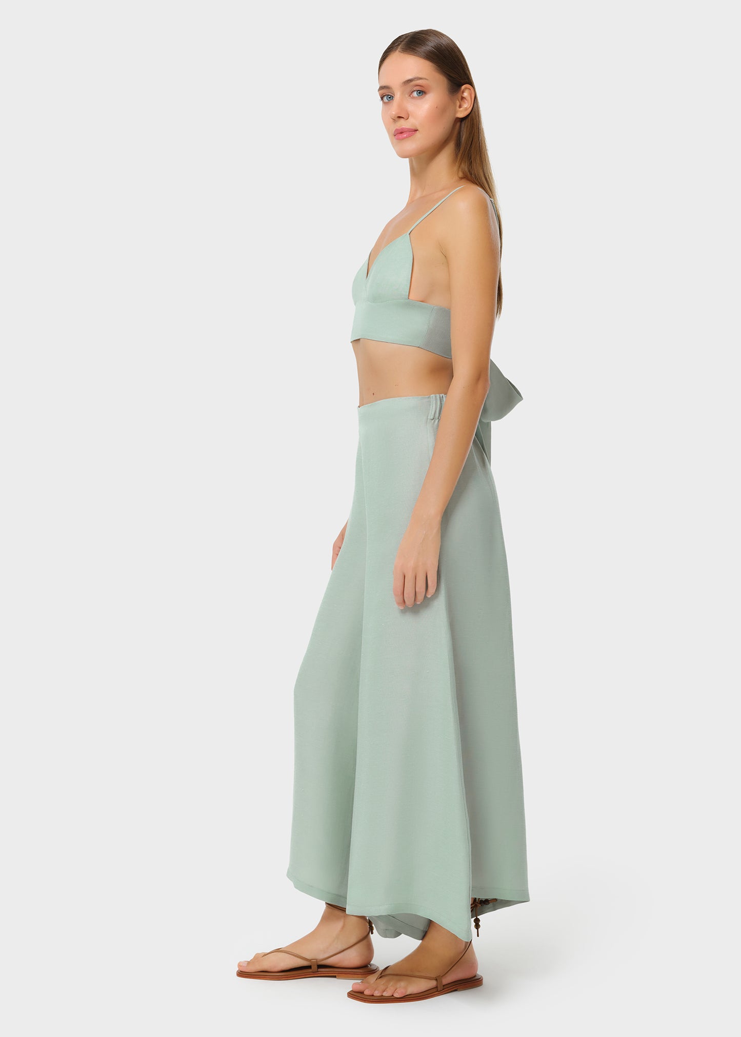 Model wearing a sage green bralette with matching high-waisted wide-leg pants, styled with flat sandals, three-quarter side view on studio background