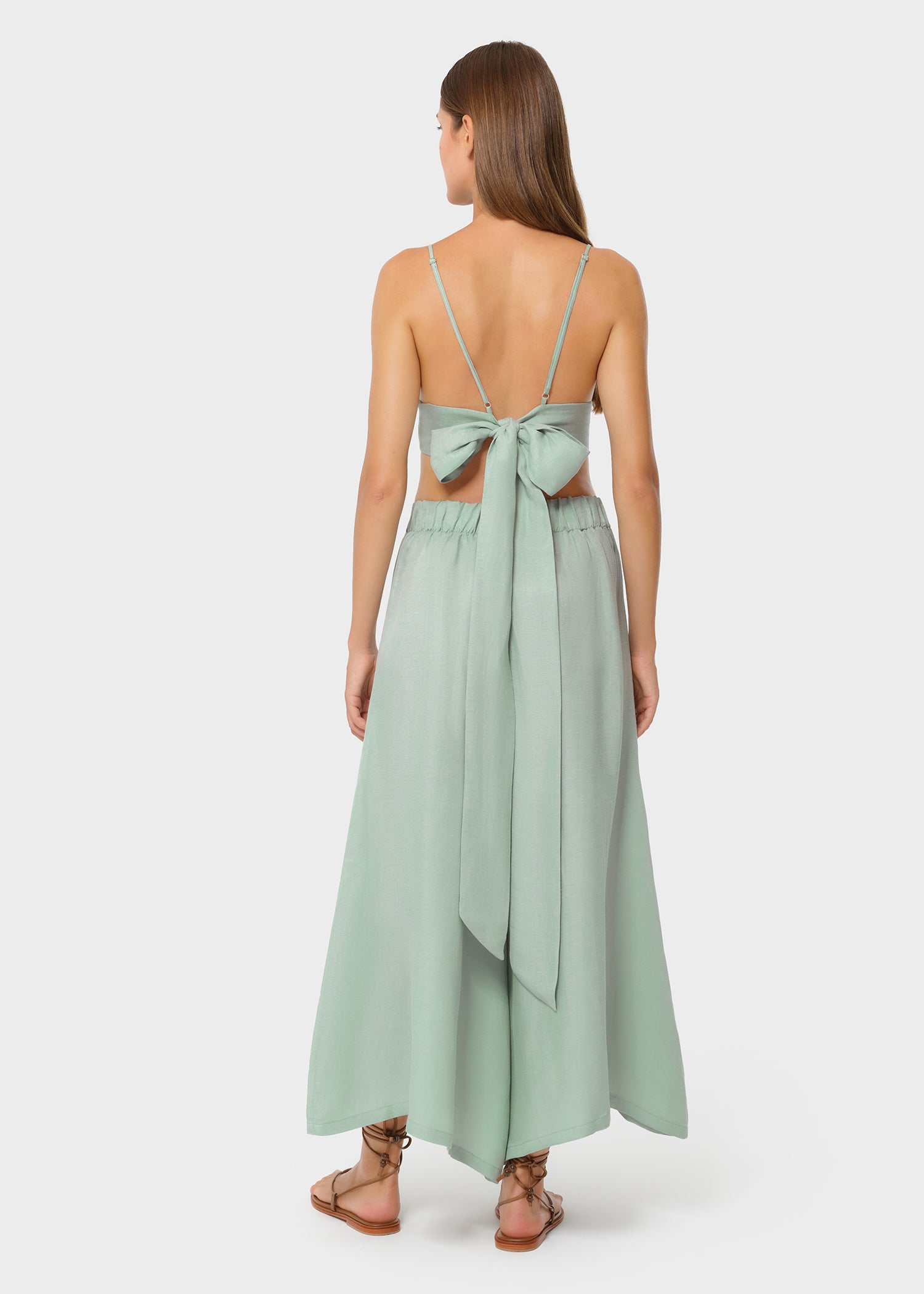 Model wearing a sage green bralette with matching high-waisted wide-leg pants, back view with bow-tie detail on studio background