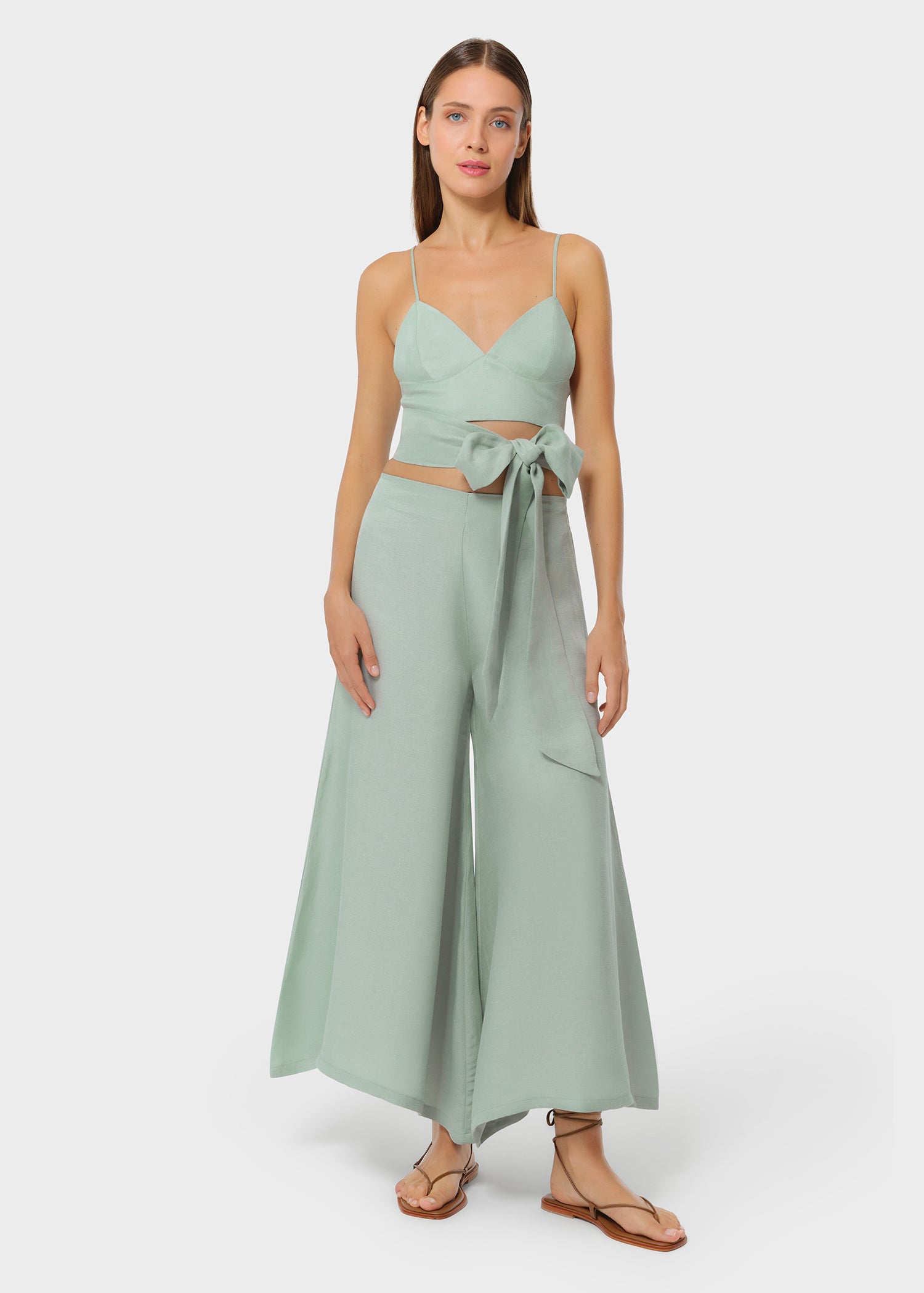 Model wearing a sage green bralette with matching high-waisted wide-leg pants, front view with side bow detail on studio background
