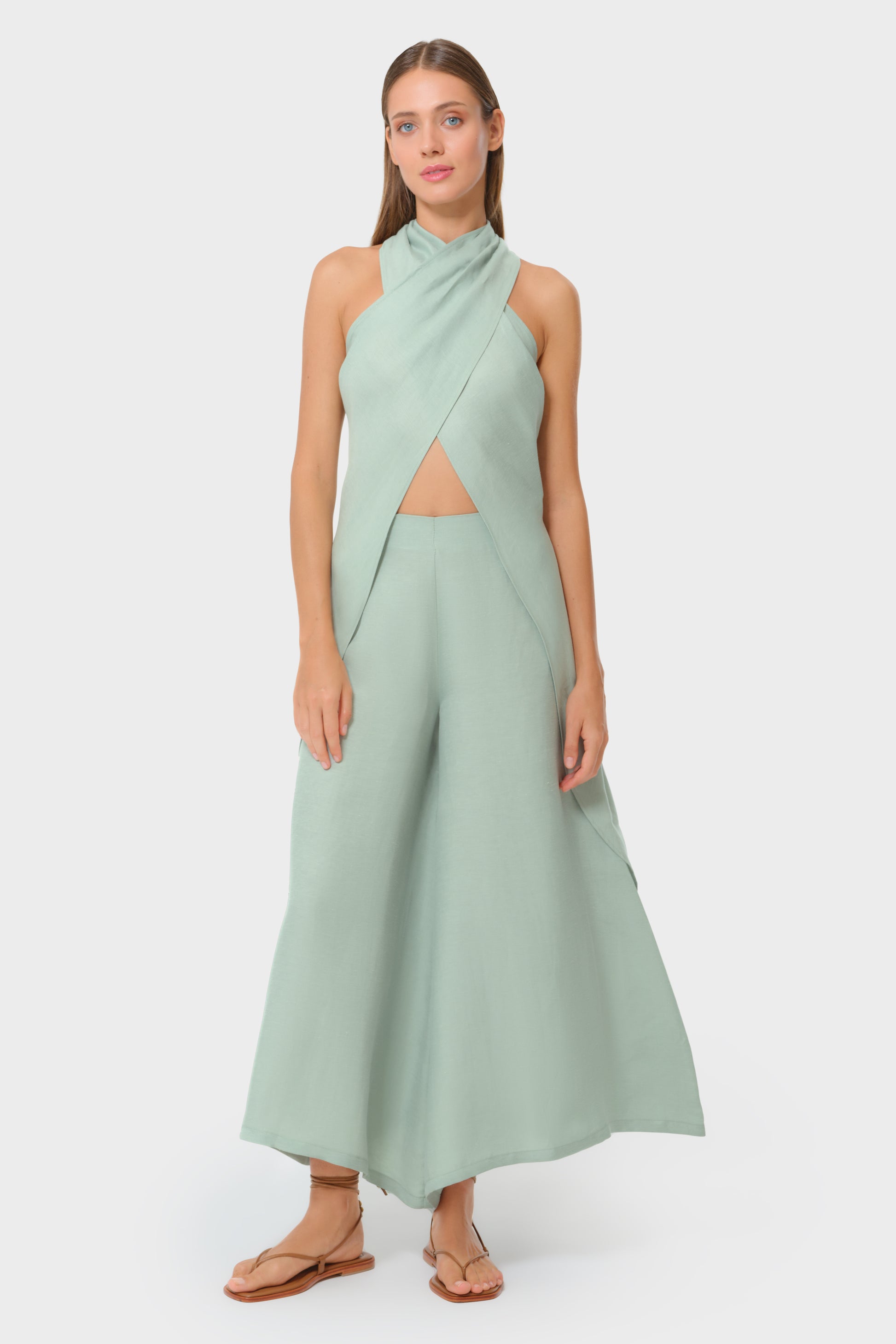 Woman wearing mint green vegan silk halter wrap top with matching wide leg pants and flat sandals, full length studio view