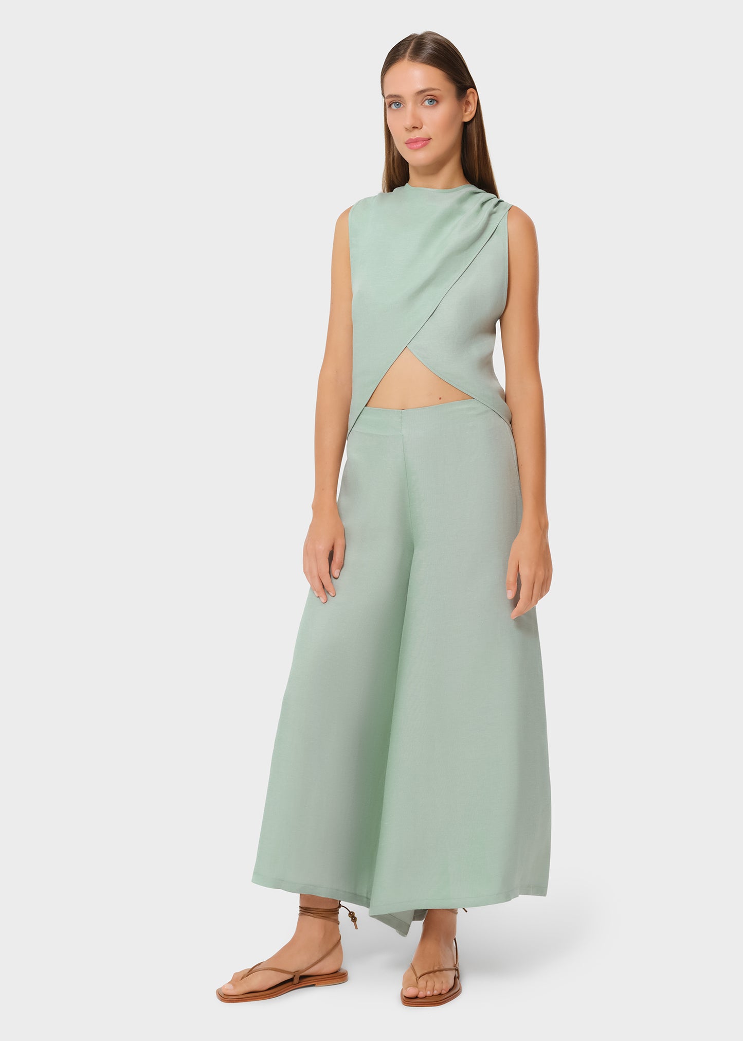 Model wearing a sage green asymmetrical wrap top with matching high-waisted wide-leg pants, front view on studio background