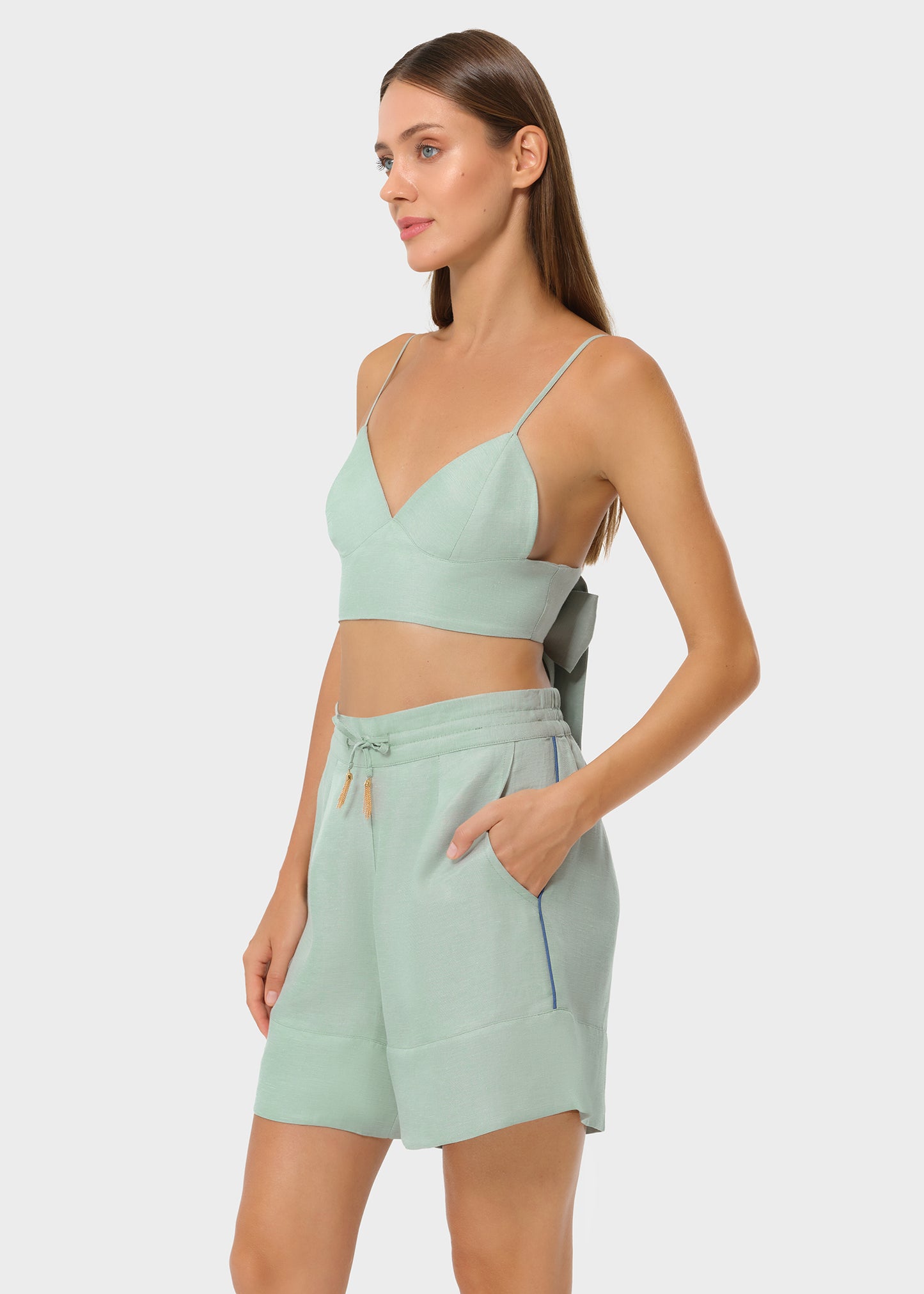Model in sage green bralette and matching lounge shorts, side view, studio background