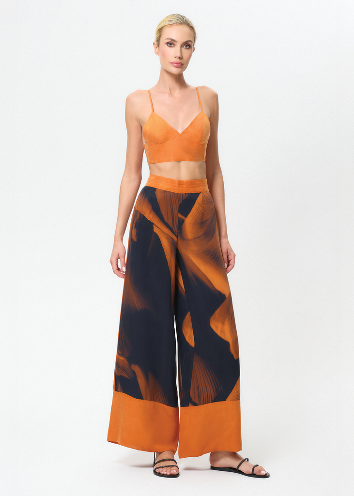 Woman wearing an orange top and patterned pants on a white background