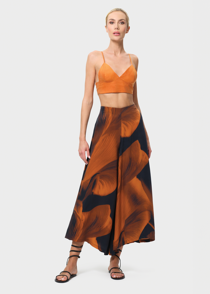 Woman wearing an orange top and patterned skirt on a white background