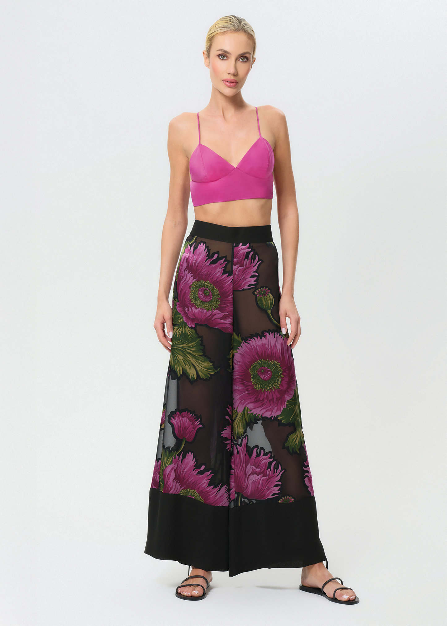 Woman wearing a pink top and black floral pant on a white background