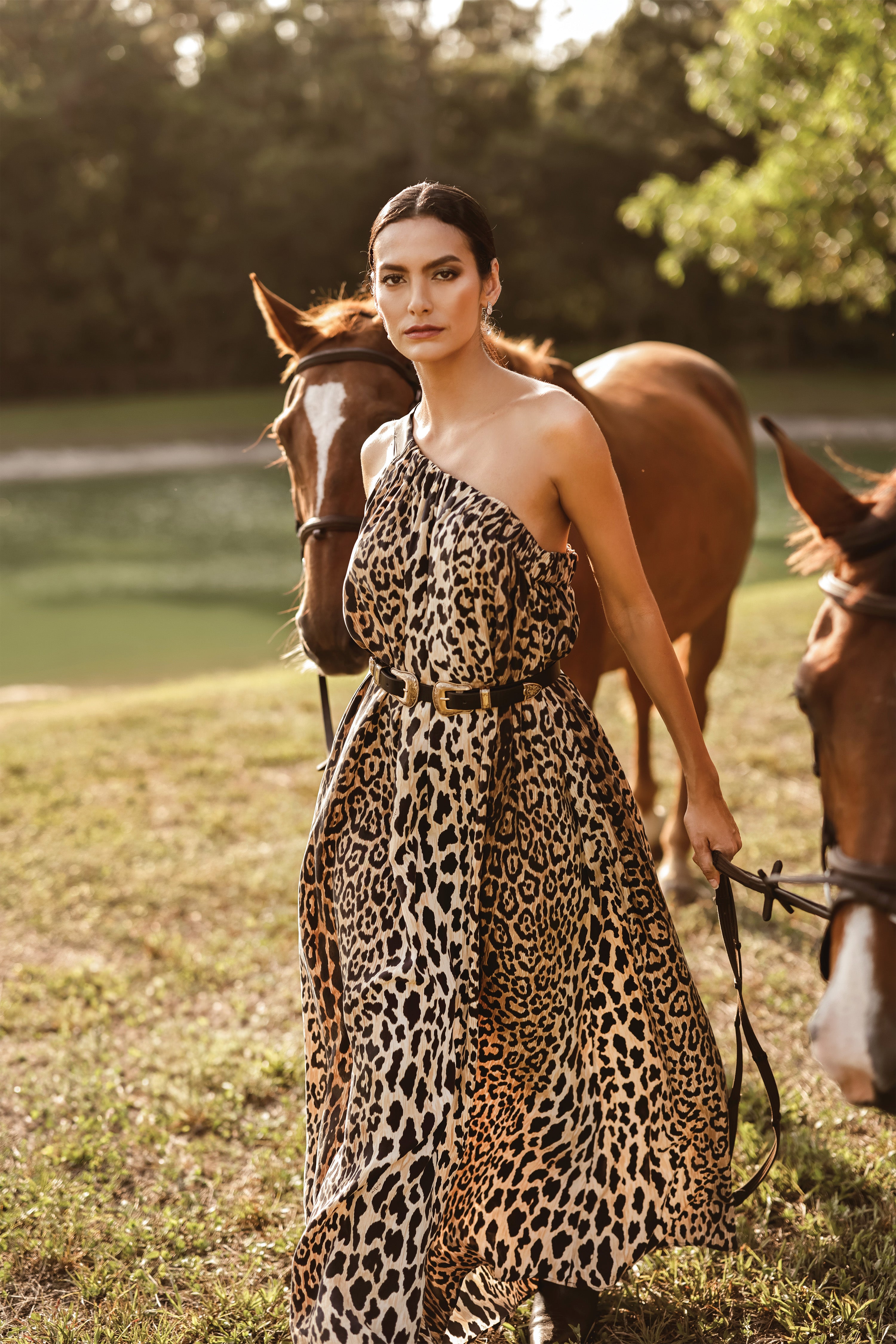 Model wearing Leo Ella one shoulder dress walking and guiding two horses.